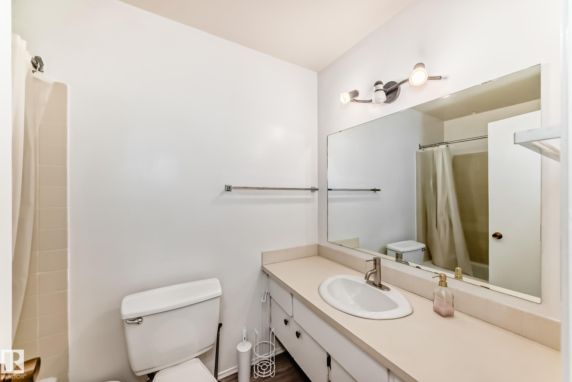 Full bathroom featuring a single vanity with an integrated sink, a large wall-mounted mirror, overhead track lighting, and a shower-tub combination with tile surround - 423 5125 Riverbend Road, Edmonton, AB - Indoor Photo Showing Bathroom
