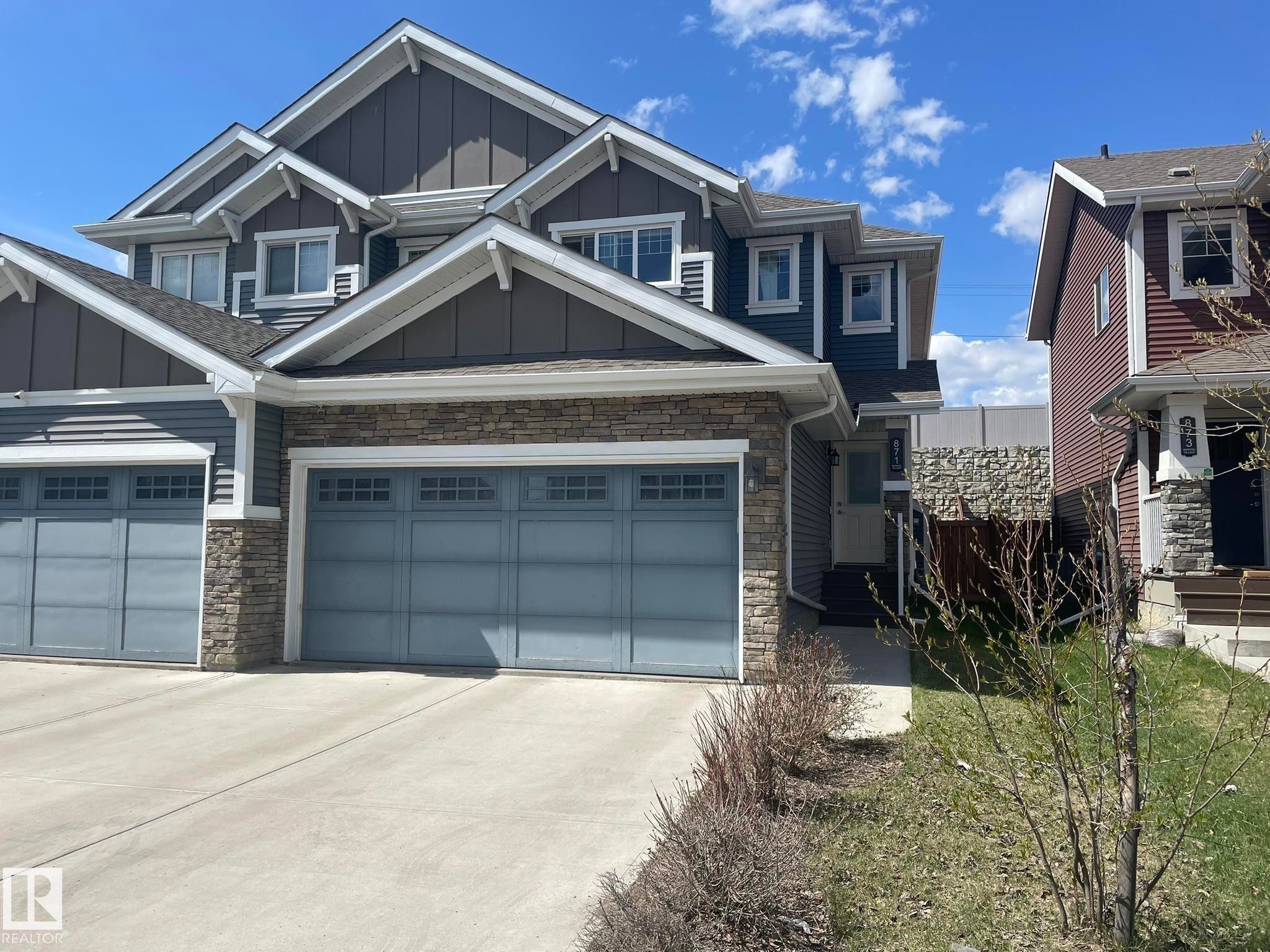 Multi-story residential exterior featuring dark gray vertical and horizontal siding, stone veneer accents, and white trim details - 871 Ebbers Crescent, Edmonton, AB - Outdoor With Facade