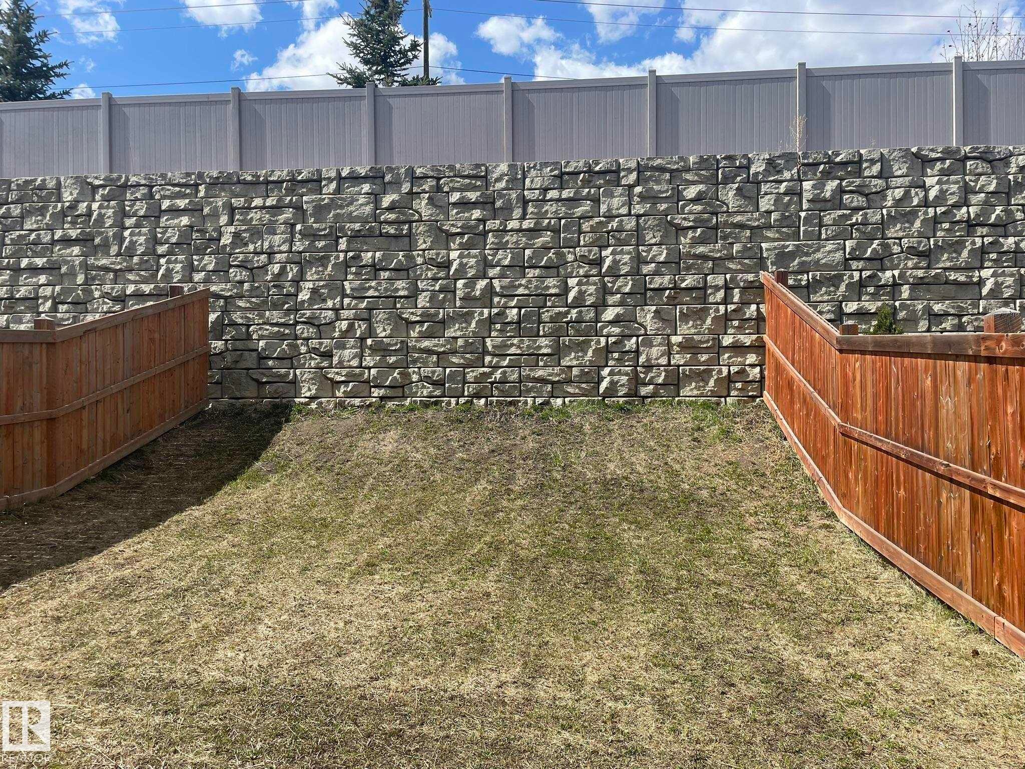 Expansive backyard featuring a stone retaining wall, two wooden fences, and a sloped grassy area - 871 Ebbers Crescent, Edmonton, AB - Outdoor
