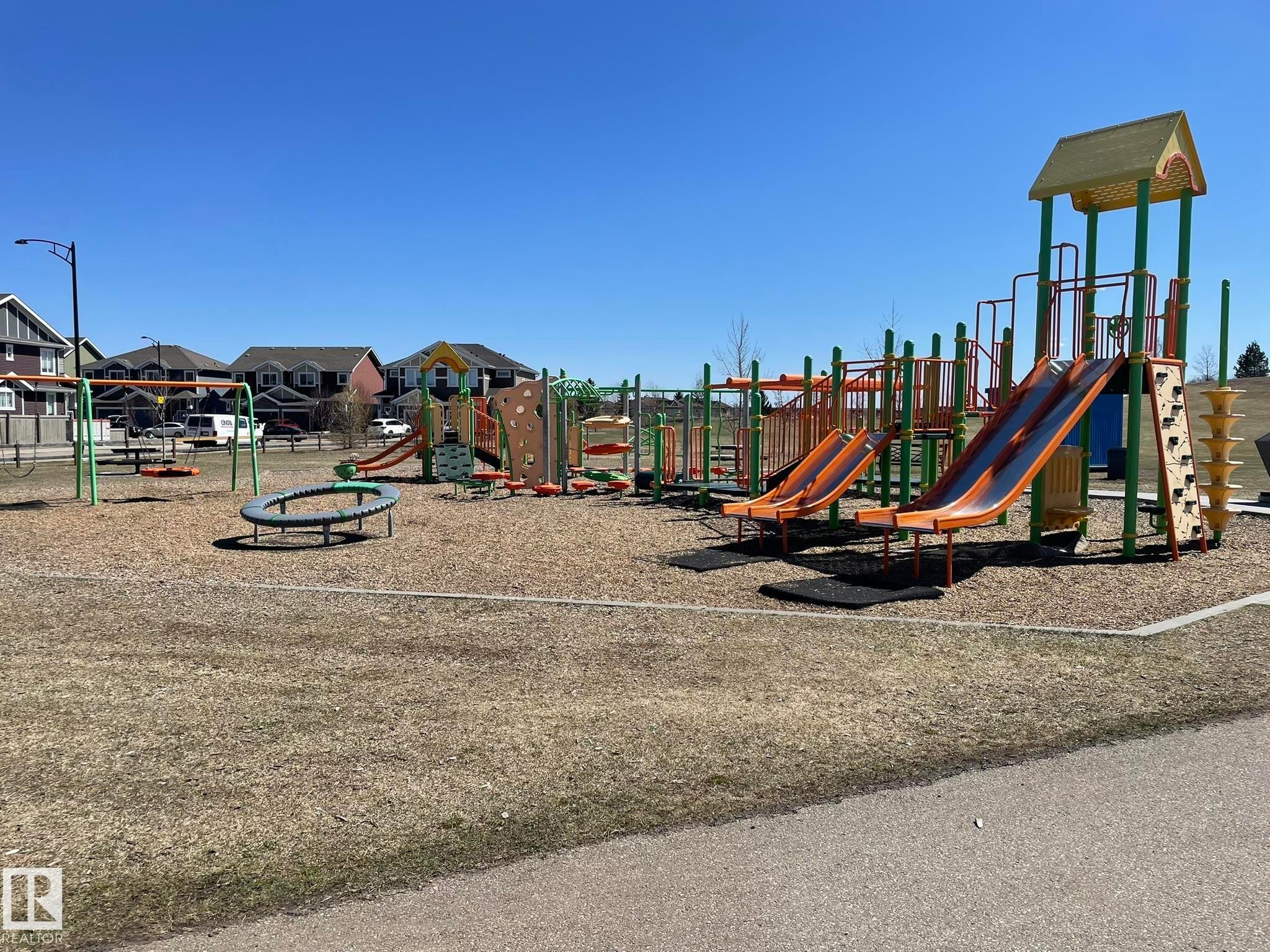 Community playground featuring multiple slides, climbing structures, a swing set, and spring riders set on wood chip surfacing - 871 Ebbers Crescent, Edmonton, AB - Outdoor