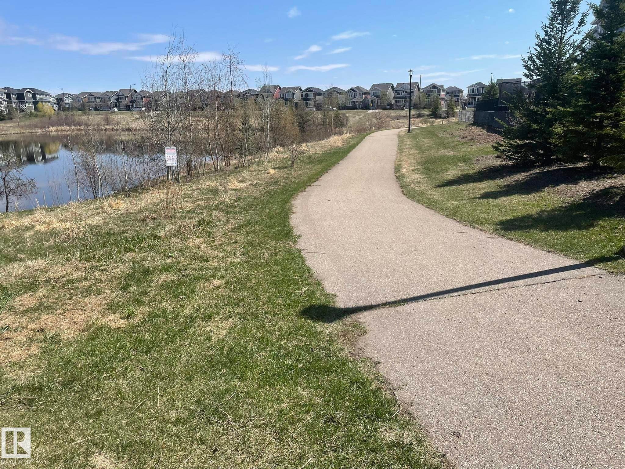 Paved pathway bordered by green grass and a body of water with residential properties in the background - 871 Ebbers Crescent, Edmonton, AB - Outdoor With View