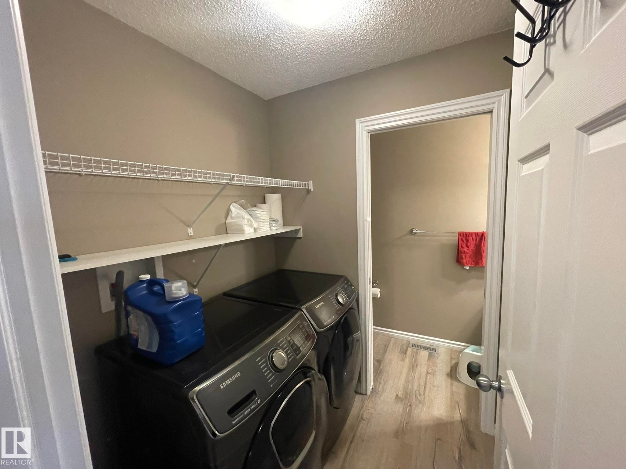 Dedicated laundry area featuring modern appliances, wall-mounted wire shelving, and wood-finish flooring - 871 Ebbers Crescent, Edmonton, AB - Indoor Photo Showing Laundry Room