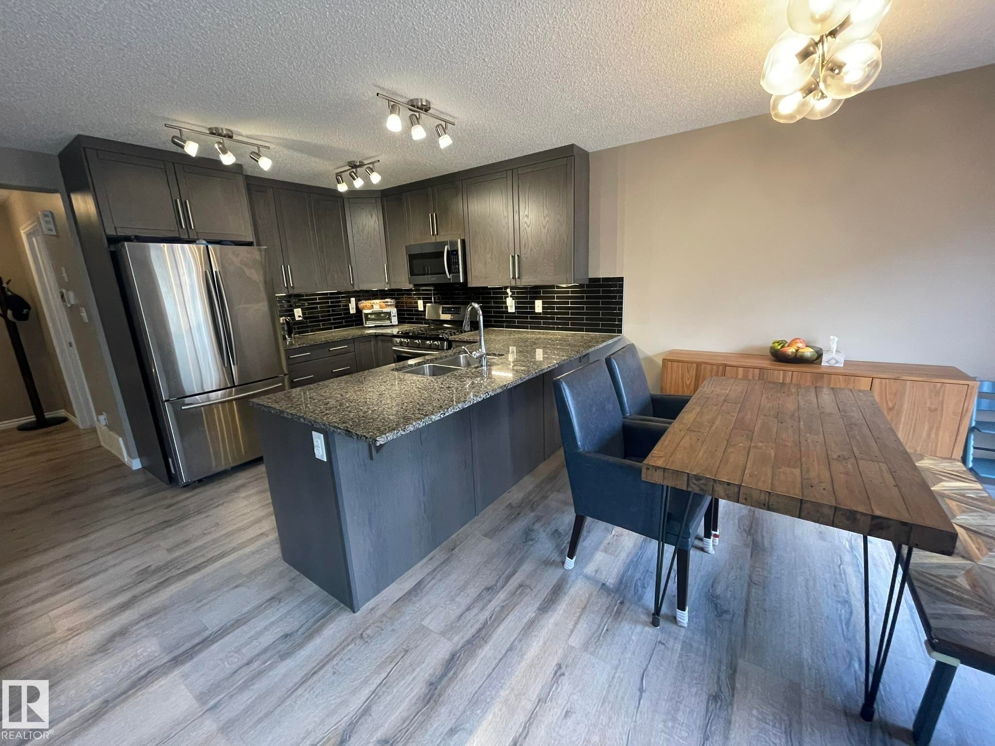 Modern kitchen featuring dark grey cabinetry, stainless steel appliances, speckled countertops, and a black subway tile backsplash - 871 Ebbers Crescent, Edmonton, AB - Indoor Photo Showing Kitchen With Double Sink