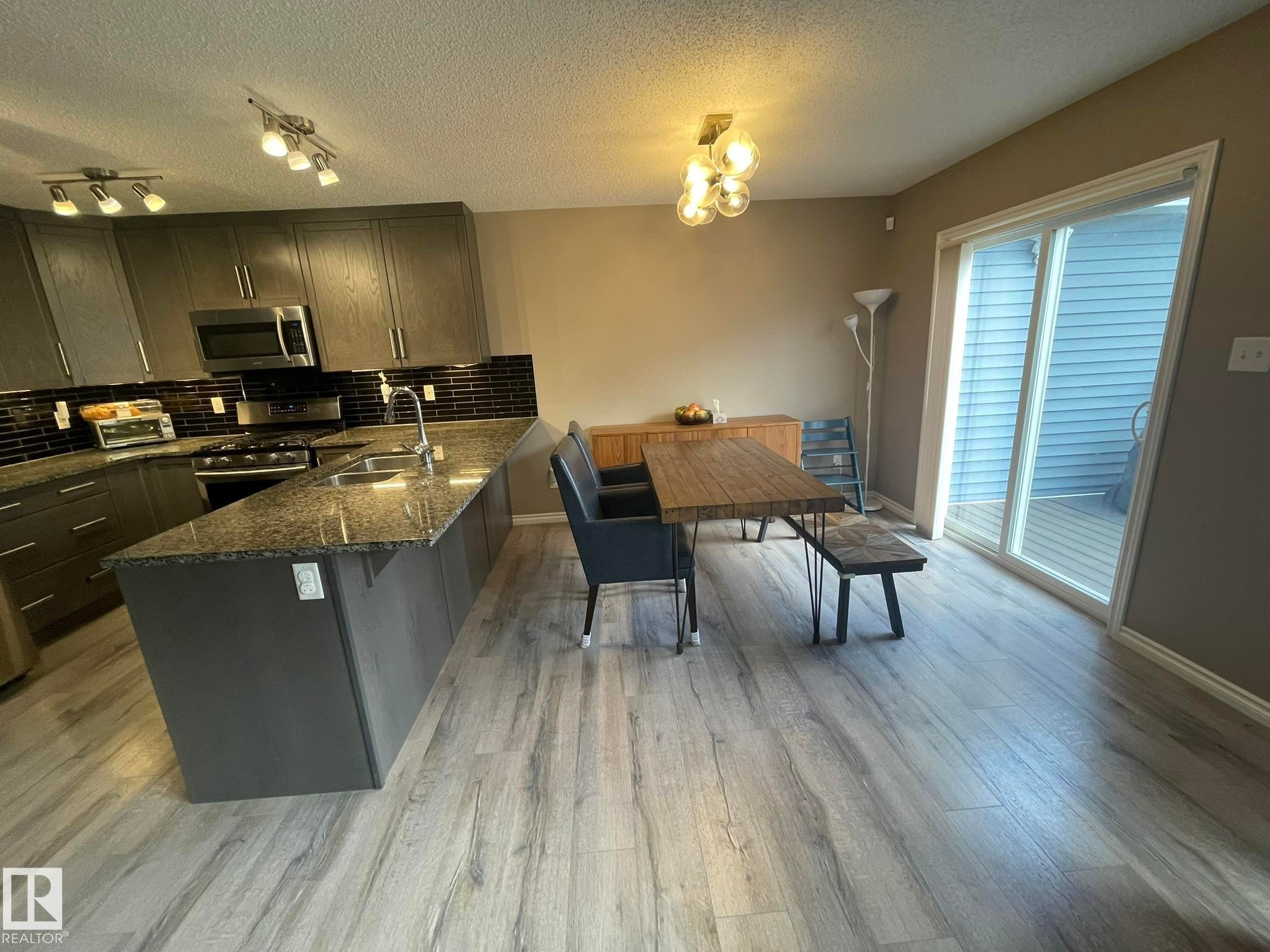 Modern kitchen featuring dark grey cabinetry, granite-style countertops, a dark subway tile backsplash, and stainless steel appliances - 871 Ebbers Crescent, Edmonton, AB - Indoor
