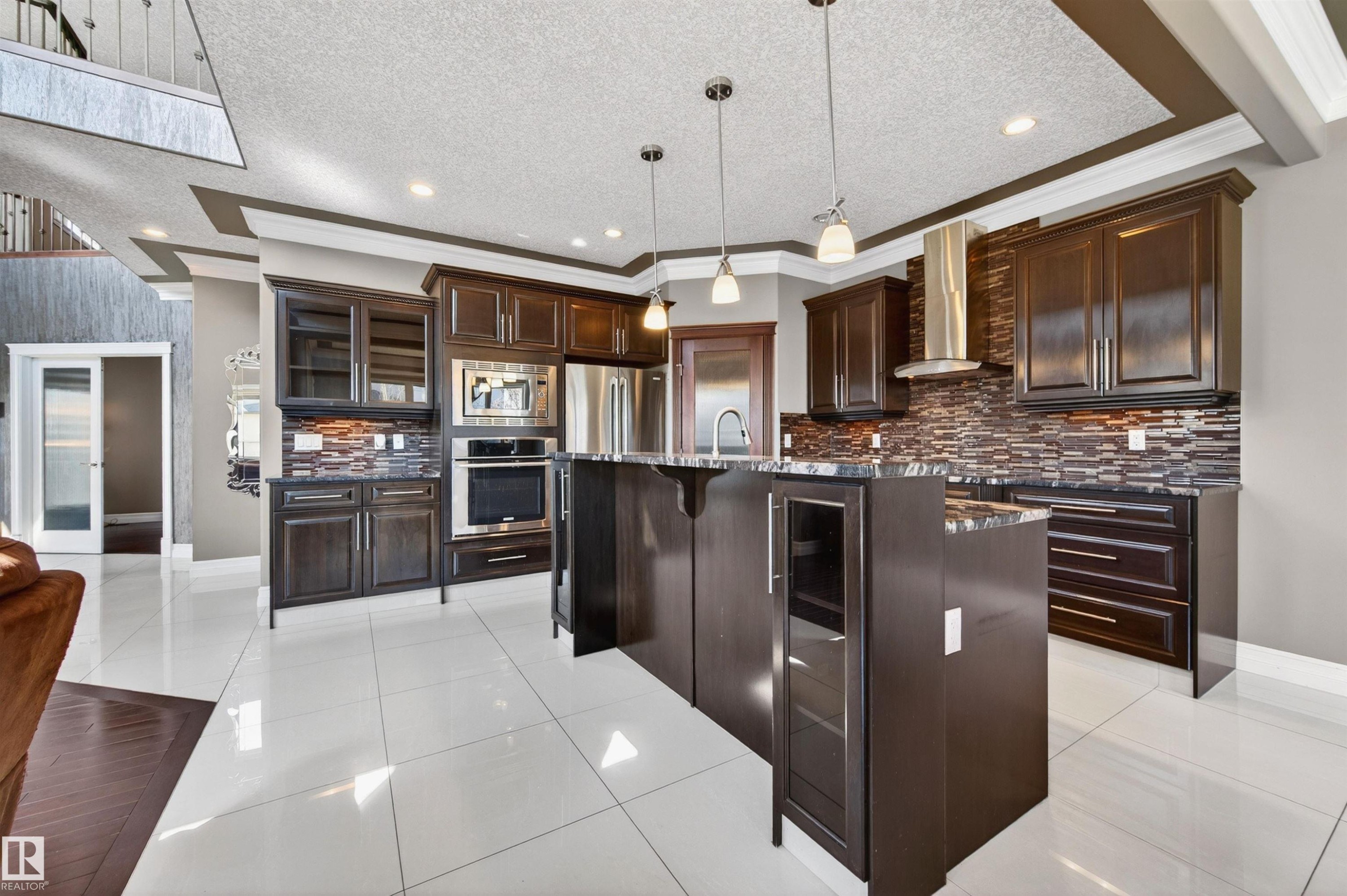 Gourmet kitchen featuring dark wood cabinetry, stainless steel appliances, a mosaic tile backsplash, a center island with pendant lighting, and white tile flooring - 1254 Adamson Drive, Edmonton, AB - Indoor Photo Showing Kitchen With Stainless Steel Kitchen With Upgraded Kitchen