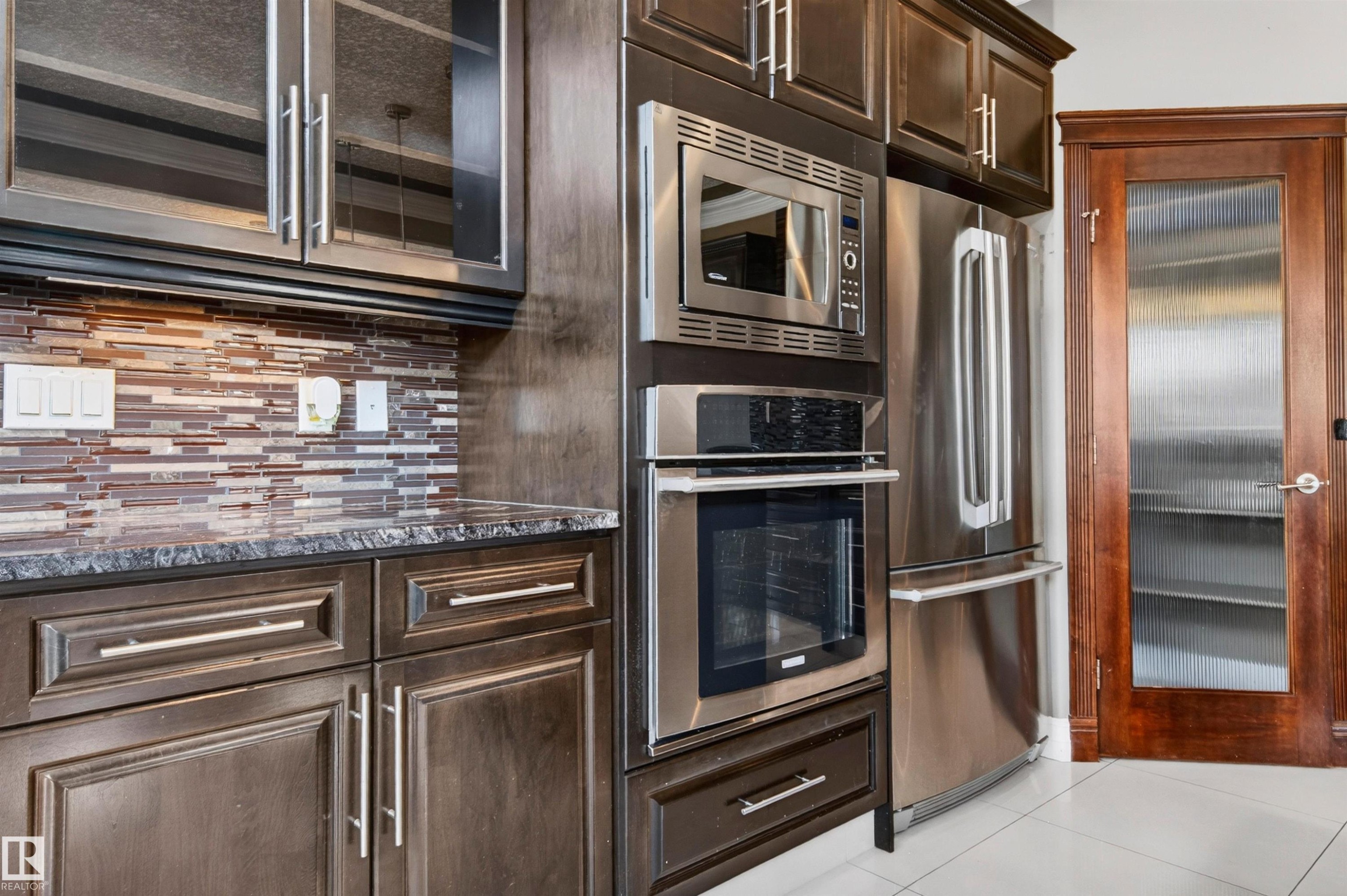 Kitchen featuring dark wood-finish cabinetry, stainless steel appliances, a mosaic tile backsplash, and a patterned countertop - 1254 Adamson Drive, Edmonton, AB - Indoor Photo Showing Kitchen With Stainless Steel Kitchen