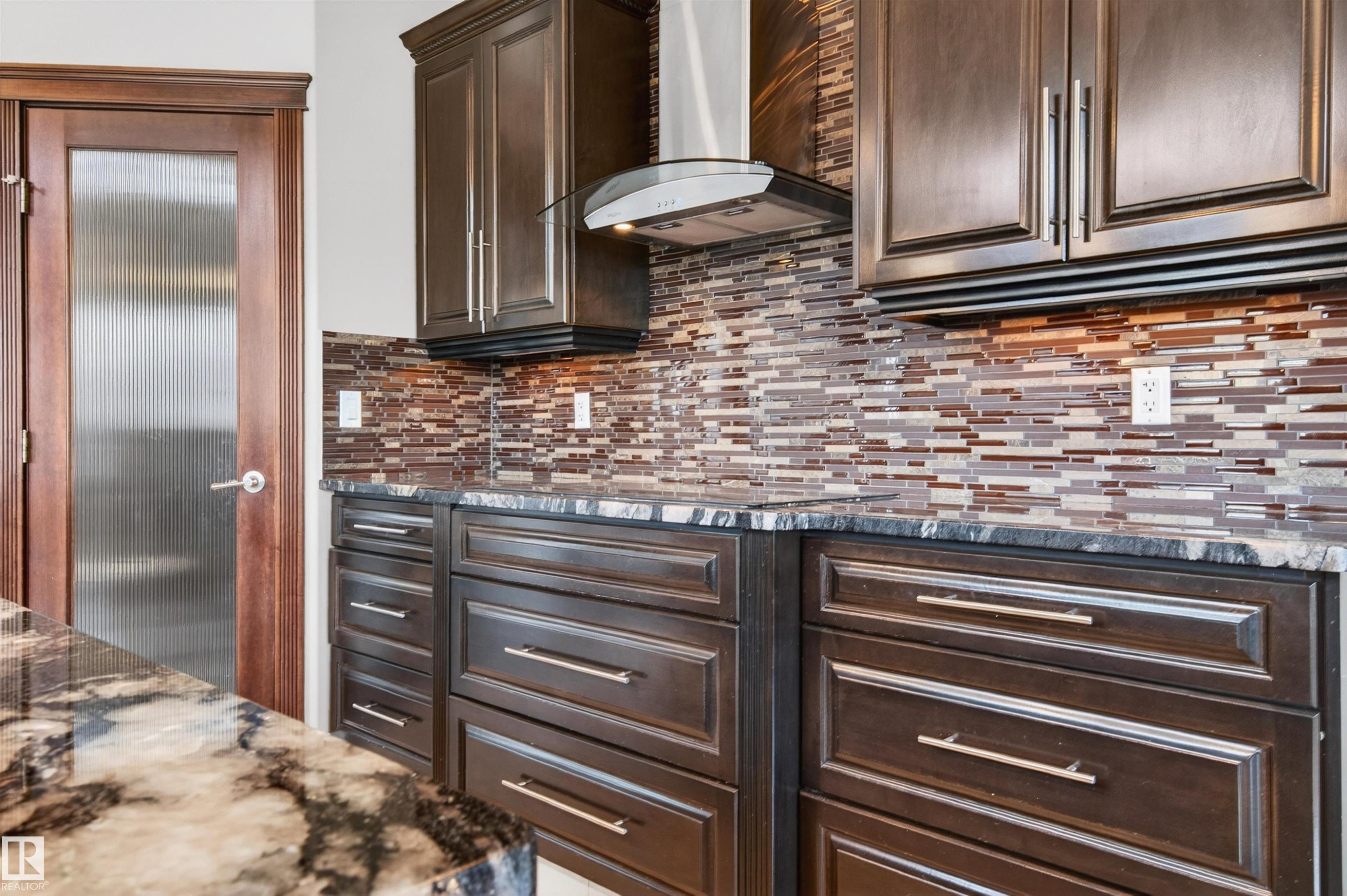 Kitchen featuring dark wood cabinetry with brushed nickel hardware, speckled countertops, and a mosaic tile backsplash - 1254 Adamson Drive, Edmonton, AB - Indoor Photo Showing Other Room
