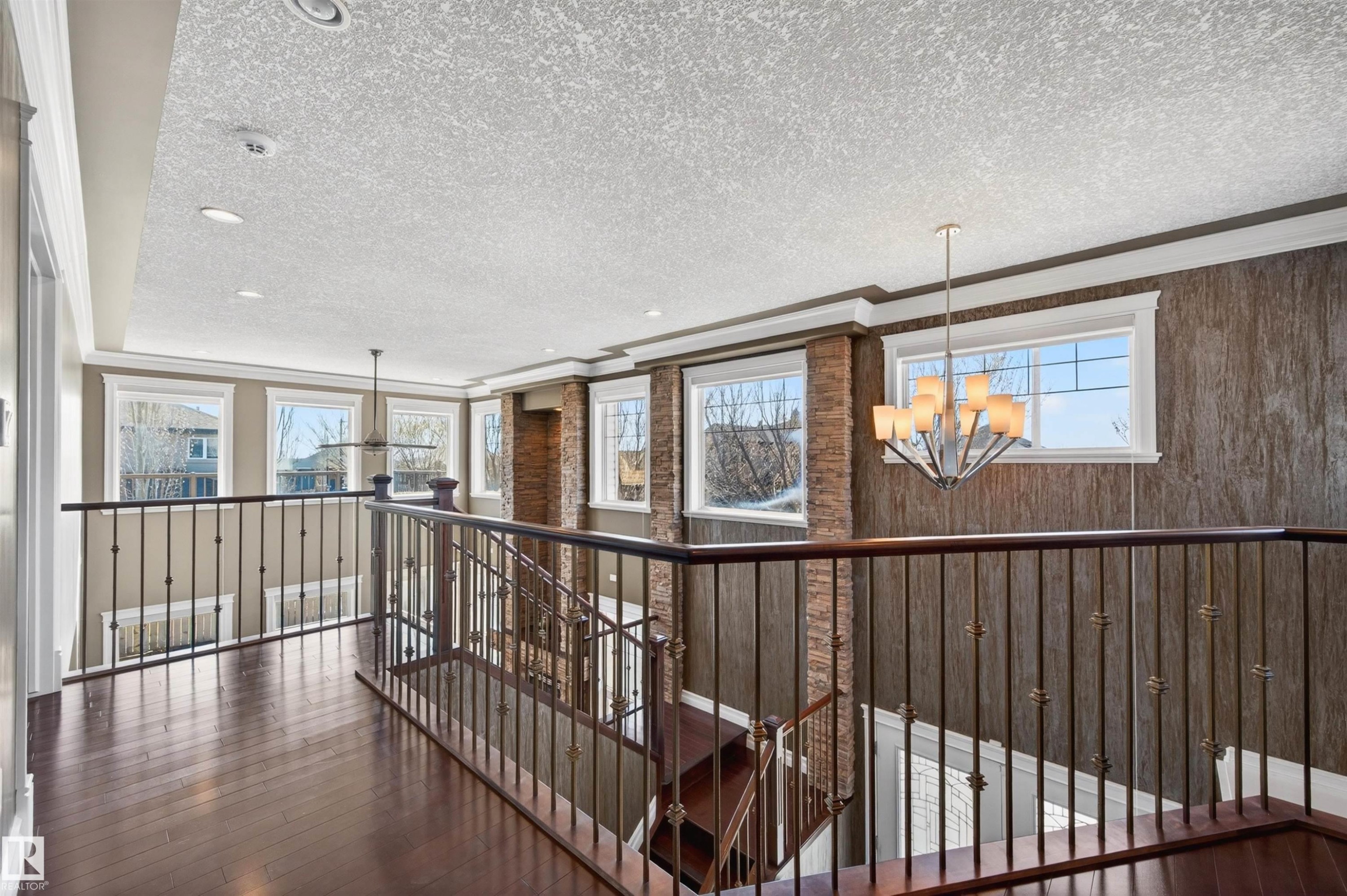 Upper-level landing featuring dark wood-finish flooring, wrought iron railings, multiple windows, recessed lighting, and a contemporary chandelier - 1254 Adamson Drive, Edmonton, AB - Indoor Photo Showing Other Room