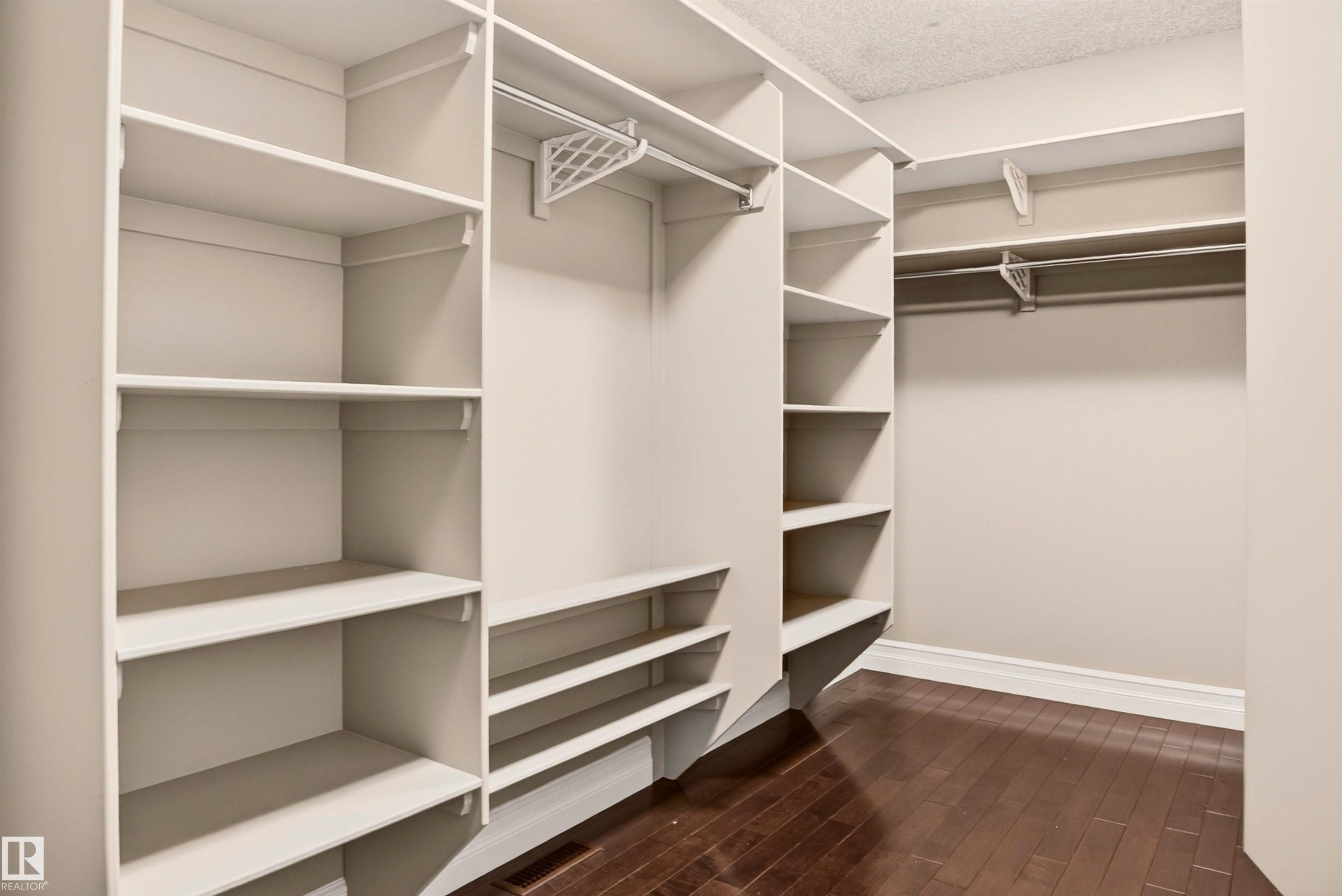 Walk-in closet with dark wood-finish flooring, built-in shelving, and multiple hanging rods - 1254 Adamson Drive, Edmonton, AB - Indoor With Storage