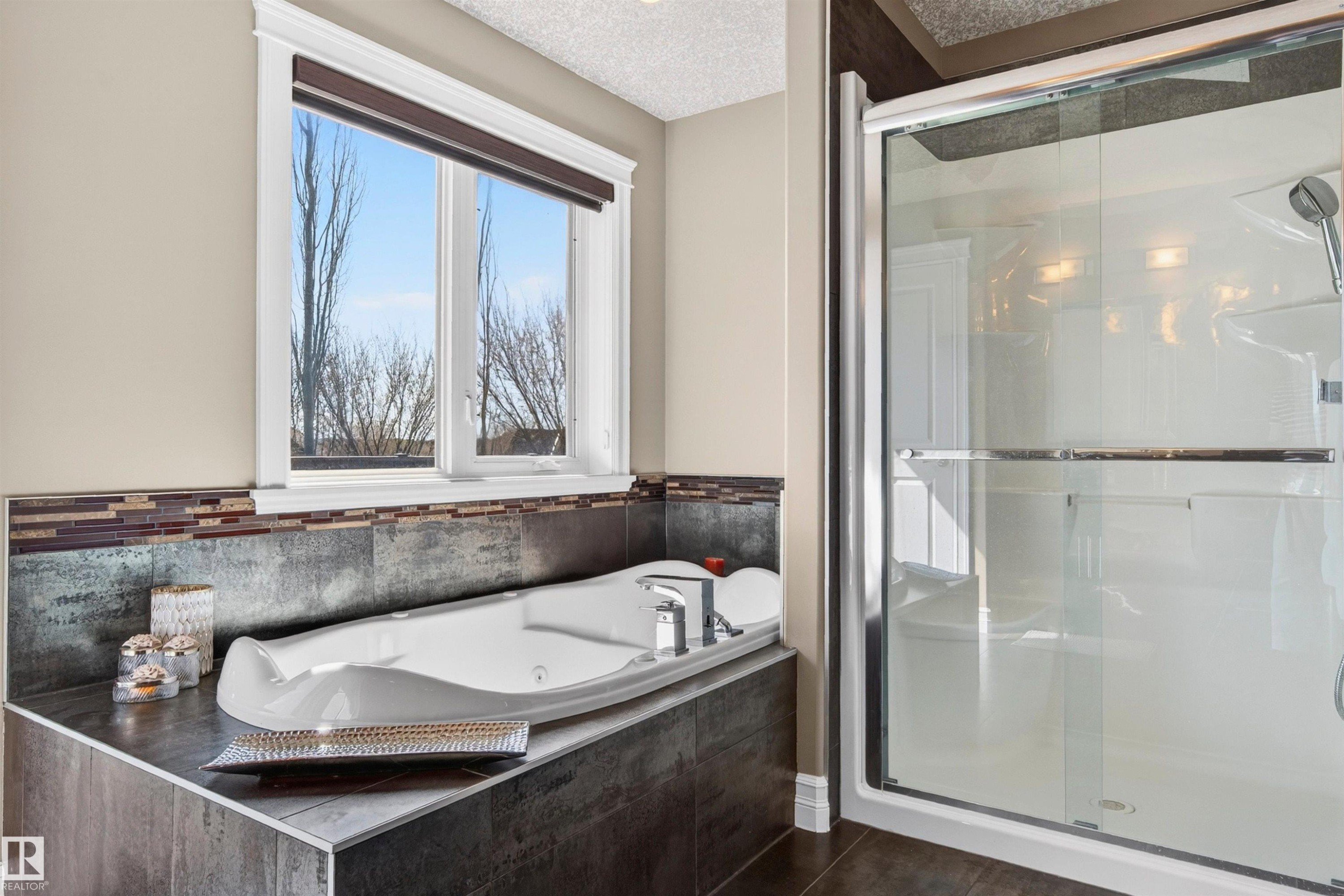 Built-in soaking tub with a tiled surround, framed window, and a glass-enclosed shower with a handheld shower fixture - 1254 Adamson Drive, Edmonton, AB - Indoor Photo Showing Bathroom