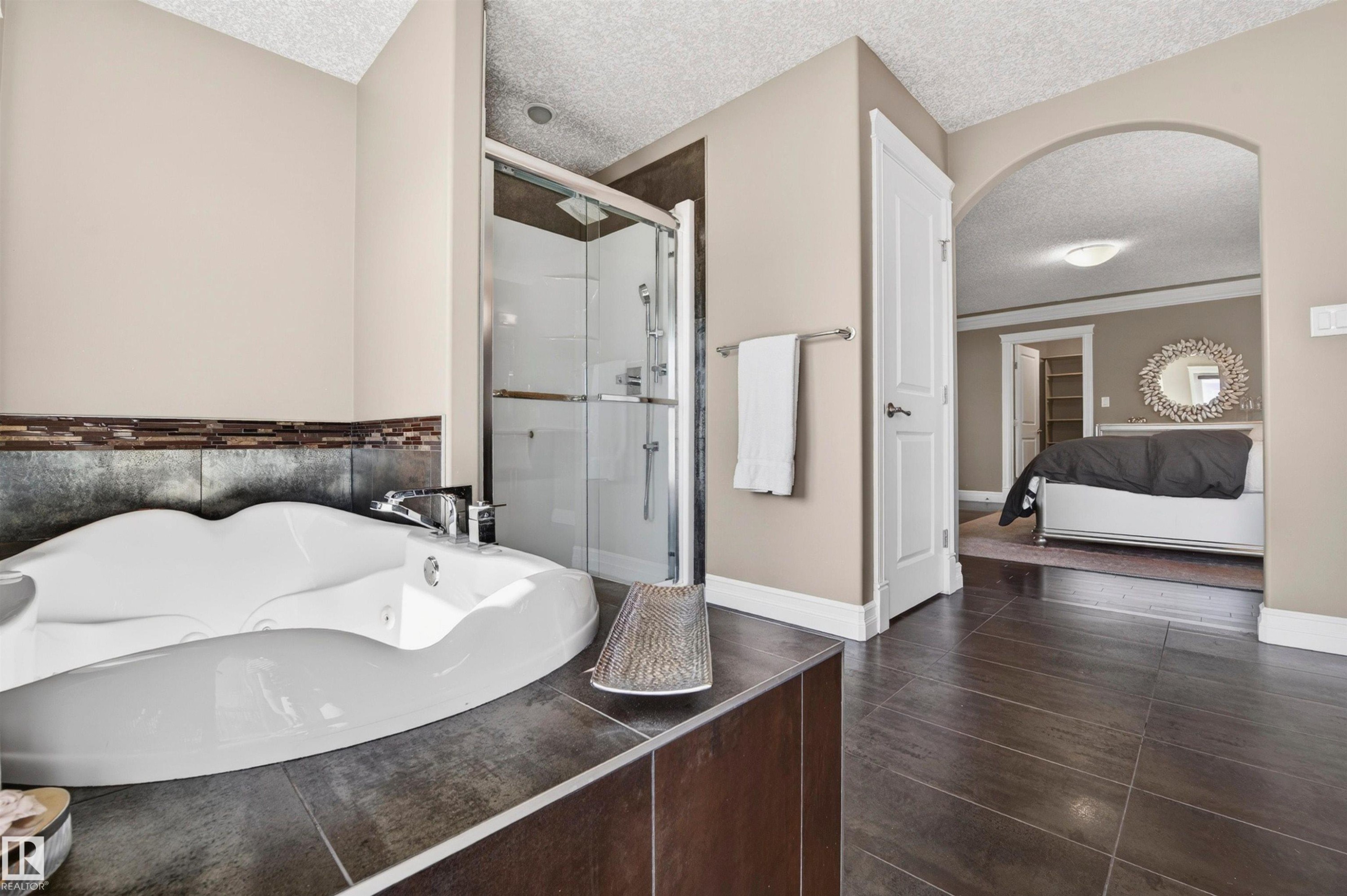 Bathroom featuring a built-in jetted tub with tile surround, glass-enclosed shower, dark large-format floor tiles, and a wide arched doorway - 1254 Adamson Drive, Edmonton, AB - Indoor Photo Showing Other Room