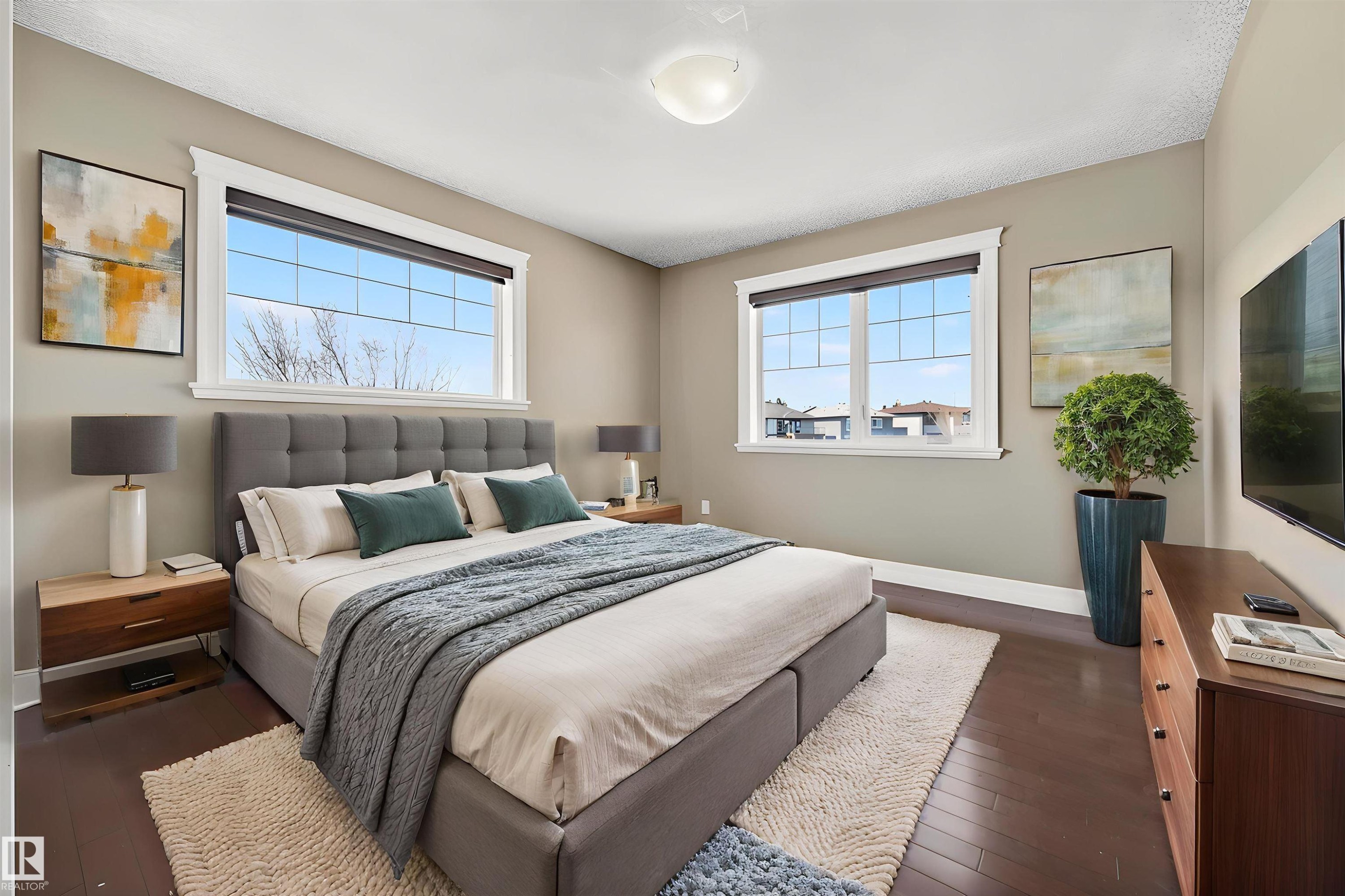 Spacious sleeping area featuring dark wood-finish flooring, two large multi-pane windows with white trim, light neutral wall paint, and a white ceiling light fixture - 1254 Adamson Drive, Edmonton, AB - Indoor Photo Showing Bedroom