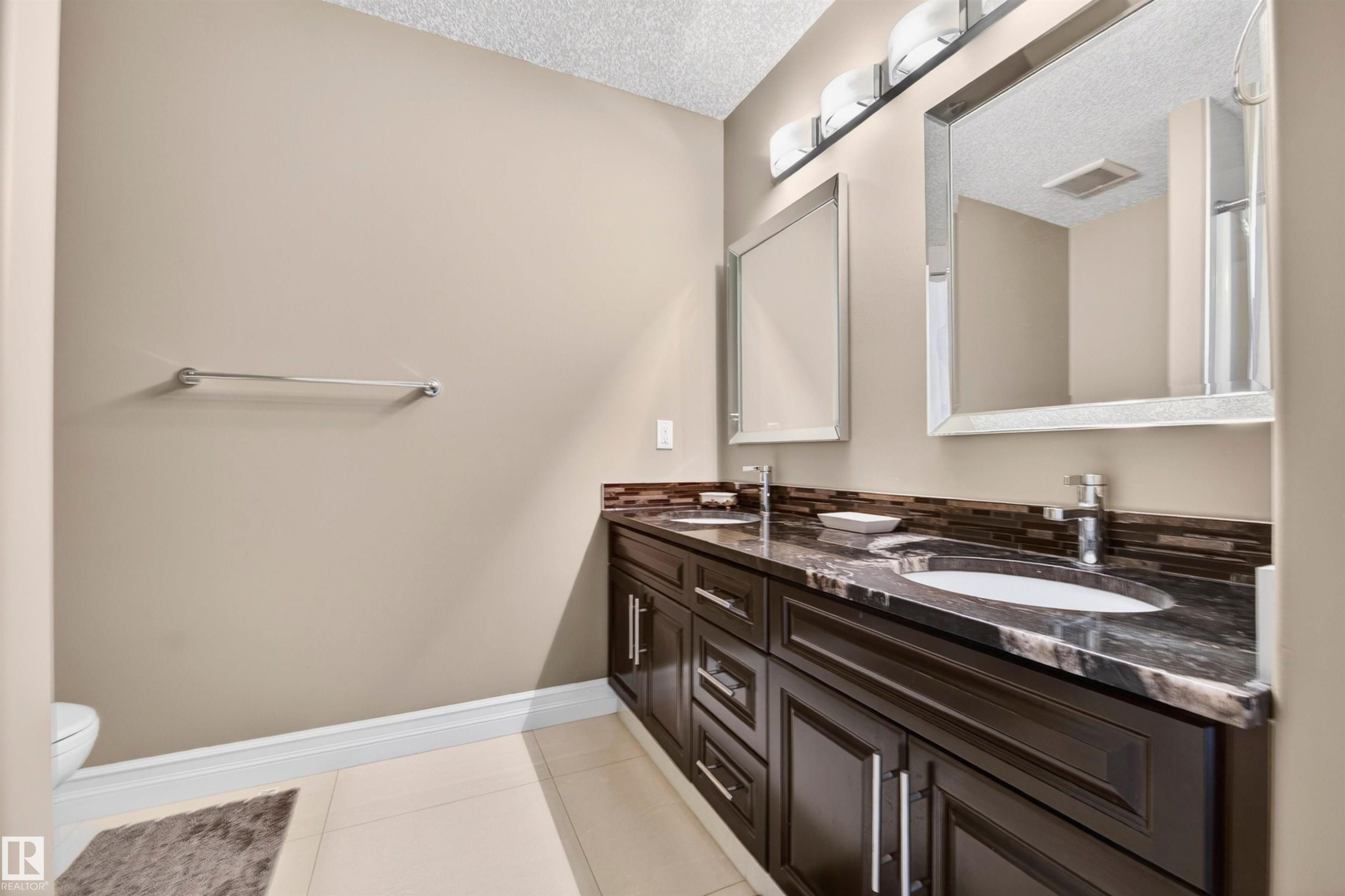 Dual sink vanity featuring dark wood cabinetry, a dark stone countertop, and two undermount sinks - 1254 Adamson Drive, Edmonton, AB - Indoor Photo Showing Bathroom