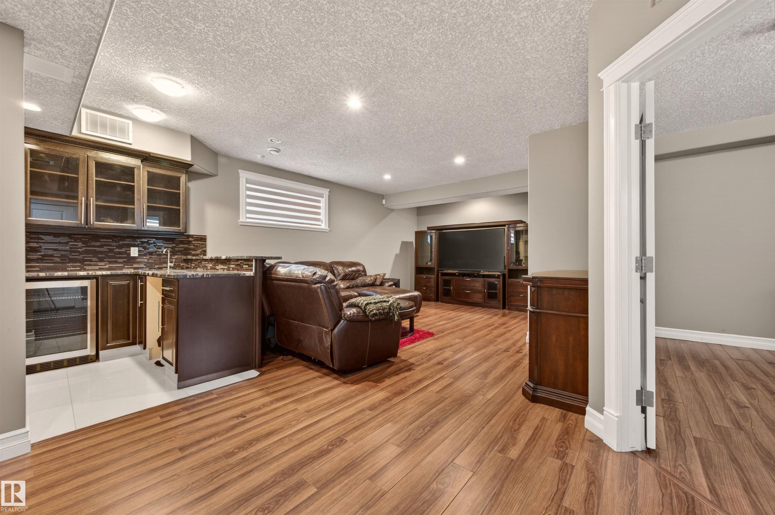 Spacious finished basement featuring wood-finish flooring, recessed lighting, and a built-in wet bar with glass-front cabinetry and an integrated beverage refrigerator - 1254 Adamson Drive, Edmonton, AB - Indoor