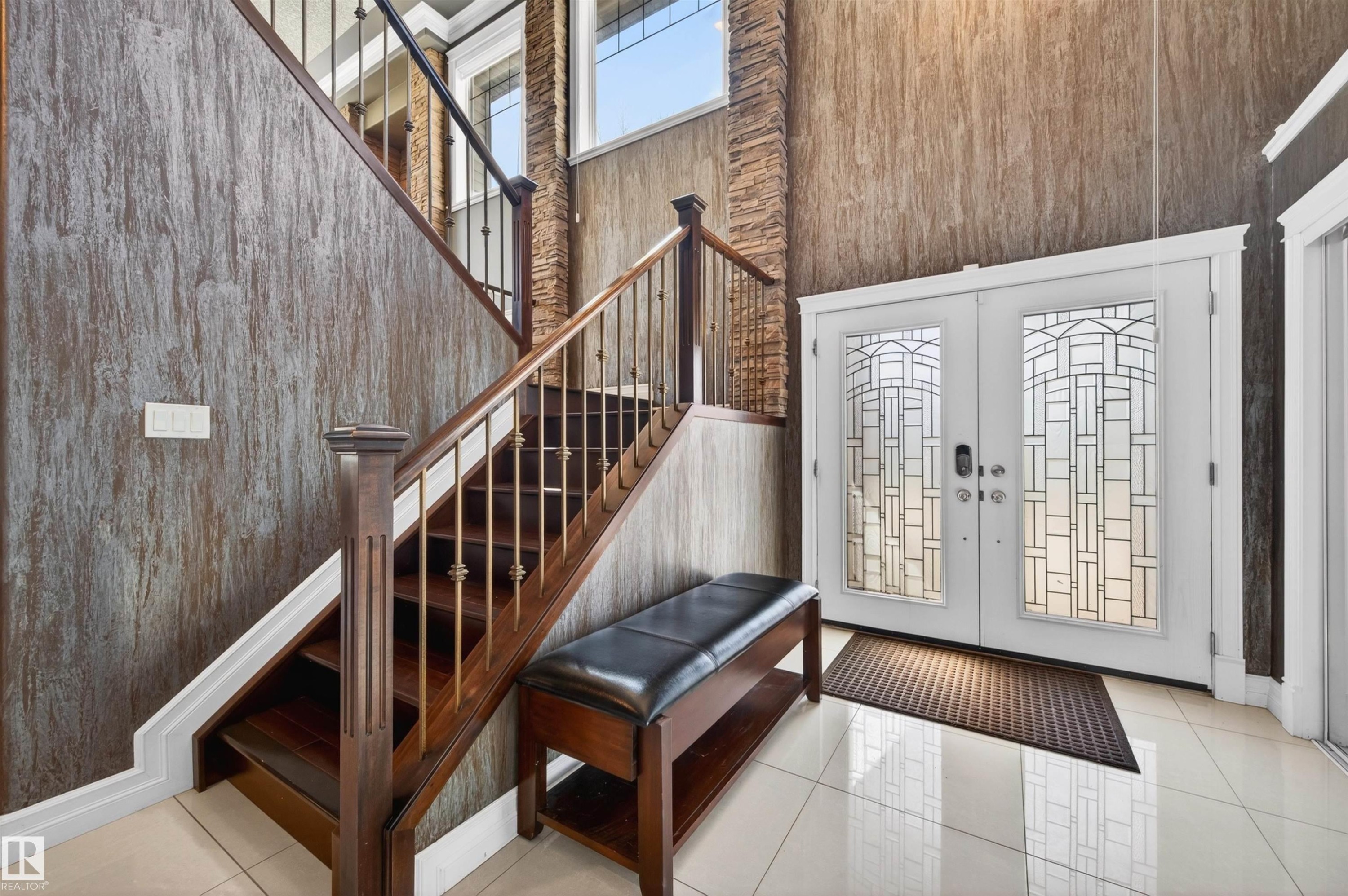 Grand foyer featuring a stained wood staircase with wrought iron balusters, stone accent wall, decorative double entry doors, and tile flooring - 1254 Adamson Drive, Edmonton, AB - Indoor Photo Showing Other Room