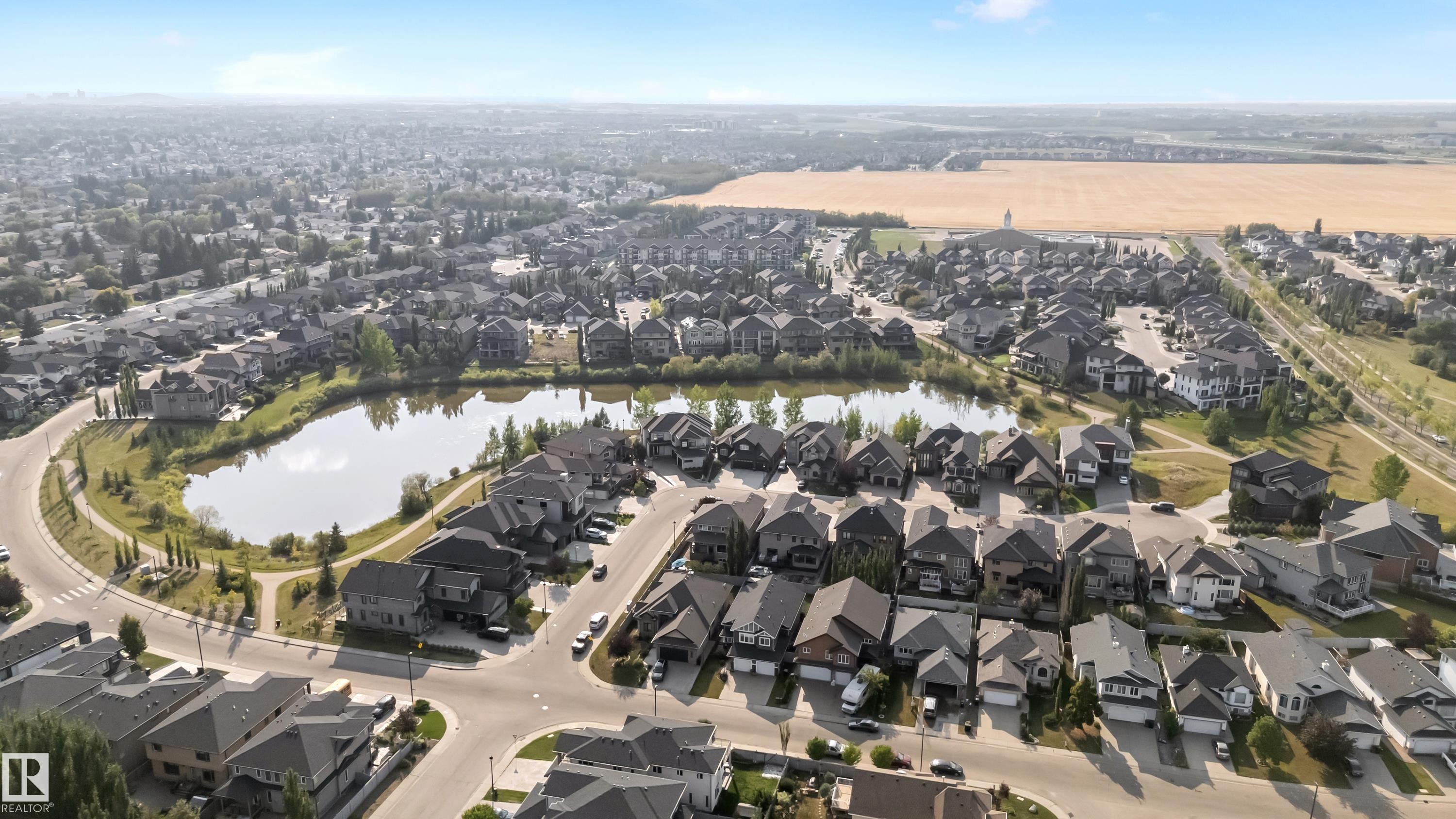 Residential neighborhood featuring a central pond, surrounding homes with diverse architectural styles, and an expansive field in the background - 10621 175A Avenue, Edmonton, AB