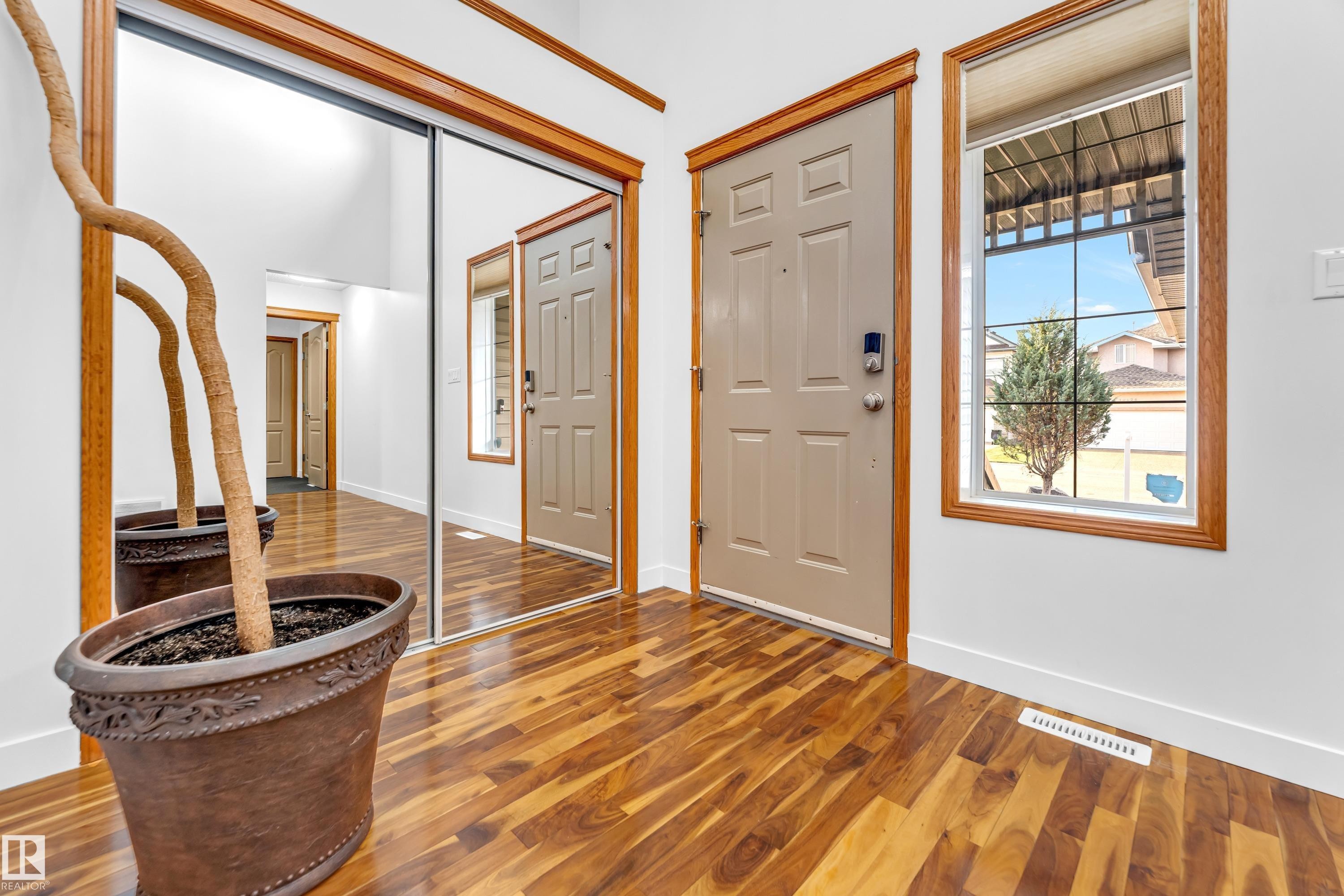 Entryway featuring wood-finish flooring, a neutral-toned door with wood trim, a side window with wood trim, and a full-height mirrored closet - 10621 175A Avenue, Edmonton, AB