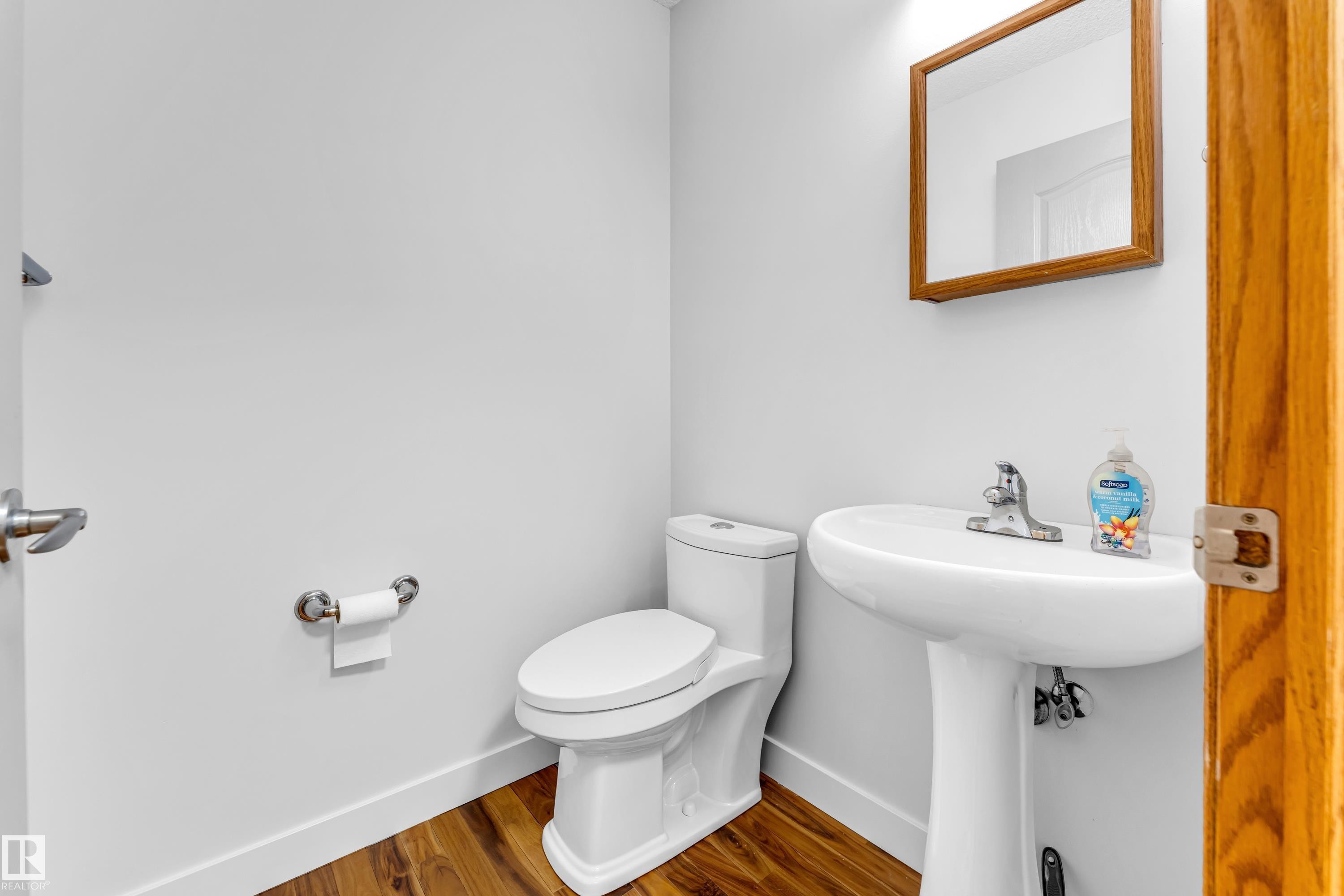 Pedestal sink with chrome faucet, complemented by a wood-finish framed mirror - 10621 175A Avenue, Edmonton, AB