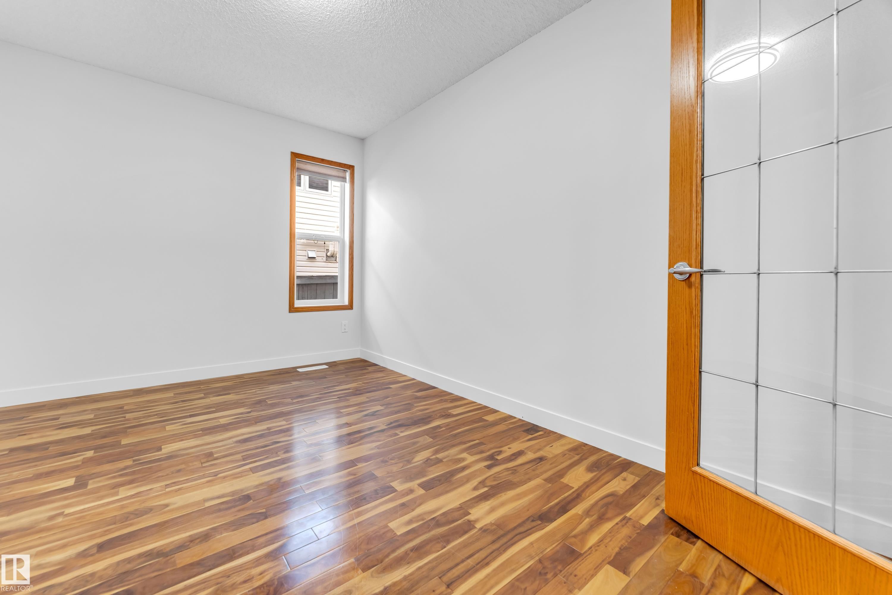 Bright interior room featuring wood-finish flooring, white walls, and a window with wood trim - 10621 175A Avenue, Edmonton, AB