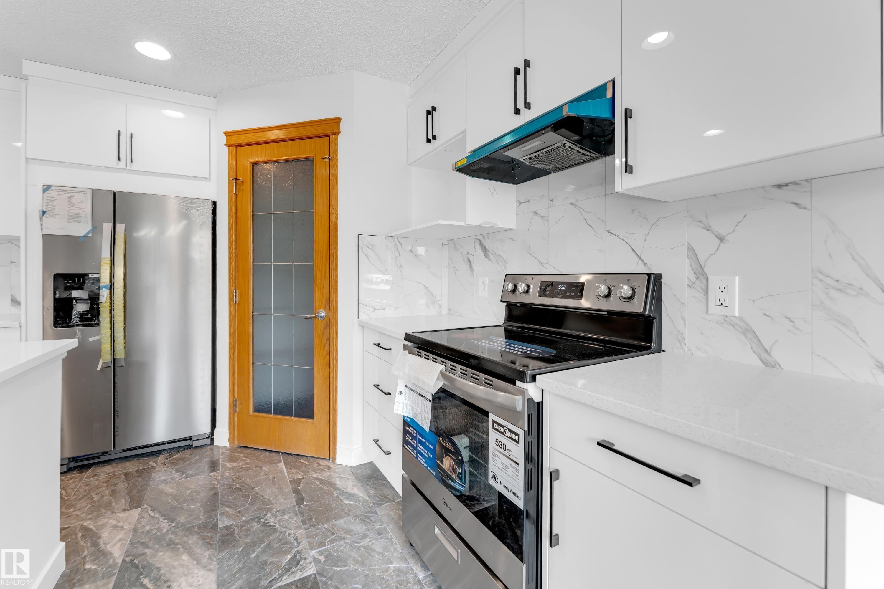 Modern kitchen featuring white cabinetry with dark hardware, a stainless steel electric range, and light-toned countertops - 10621 175A Avenue, Edmonton, AB