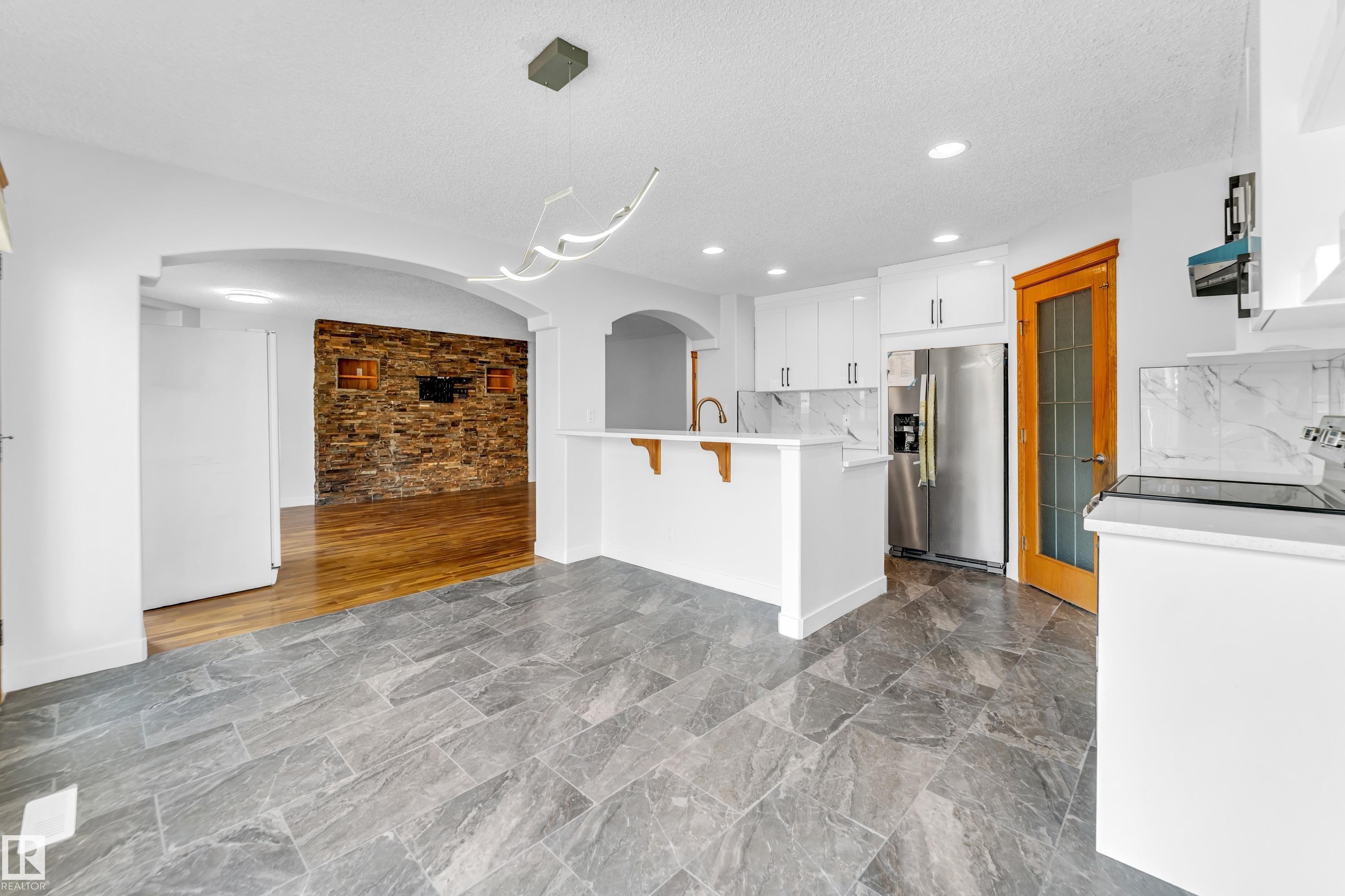 Spacious kitchen featuring white cabinetry, stainless steel appliances, a breakfast bar, and stone-look flooring - 10621 175A Avenue, Edmonton, AB