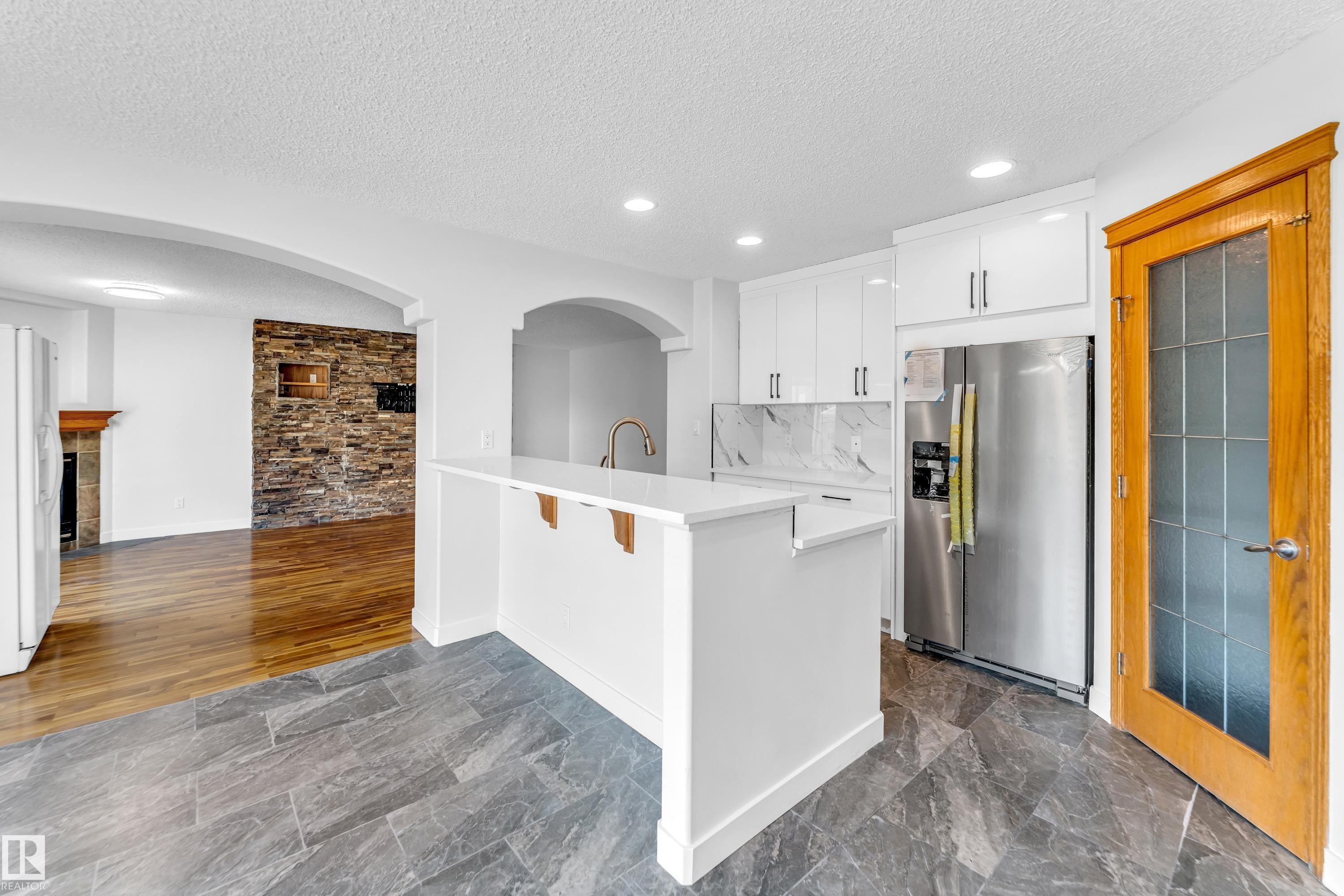 Kitchen featuring white cabinetry, stainless steel refrigerator, white countertops, and a marble-patterned backsplash - 10621 175A Avenue, Edmonton, AB