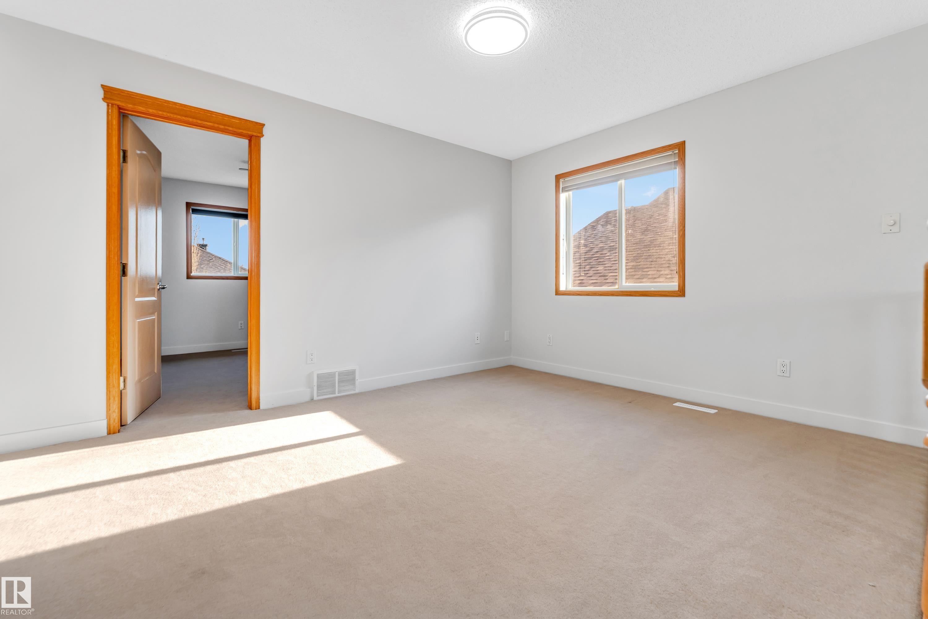 Carpeted room featuring a large window with a wood-finish frame, a mountain backdrop, a flush-mount ceiling light fixture, a wood-finish door, and white baseboards - 10621 175A Avenue, Edmonton, AB