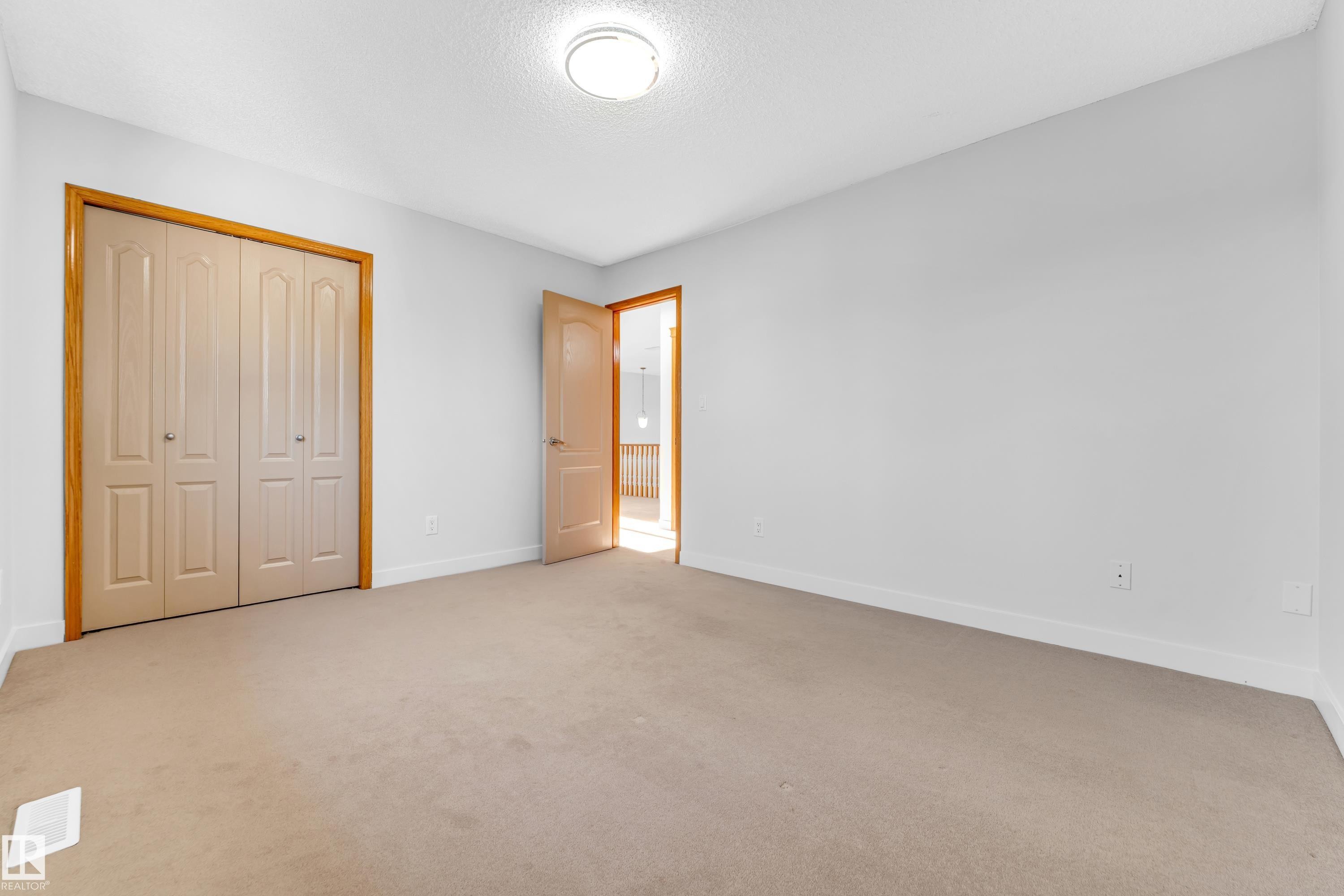 Spacious room featuring neutral carpet flooring, white walls, and a bi-fold closet with wood trim - 10621 175A Avenue, Edmonton, AB