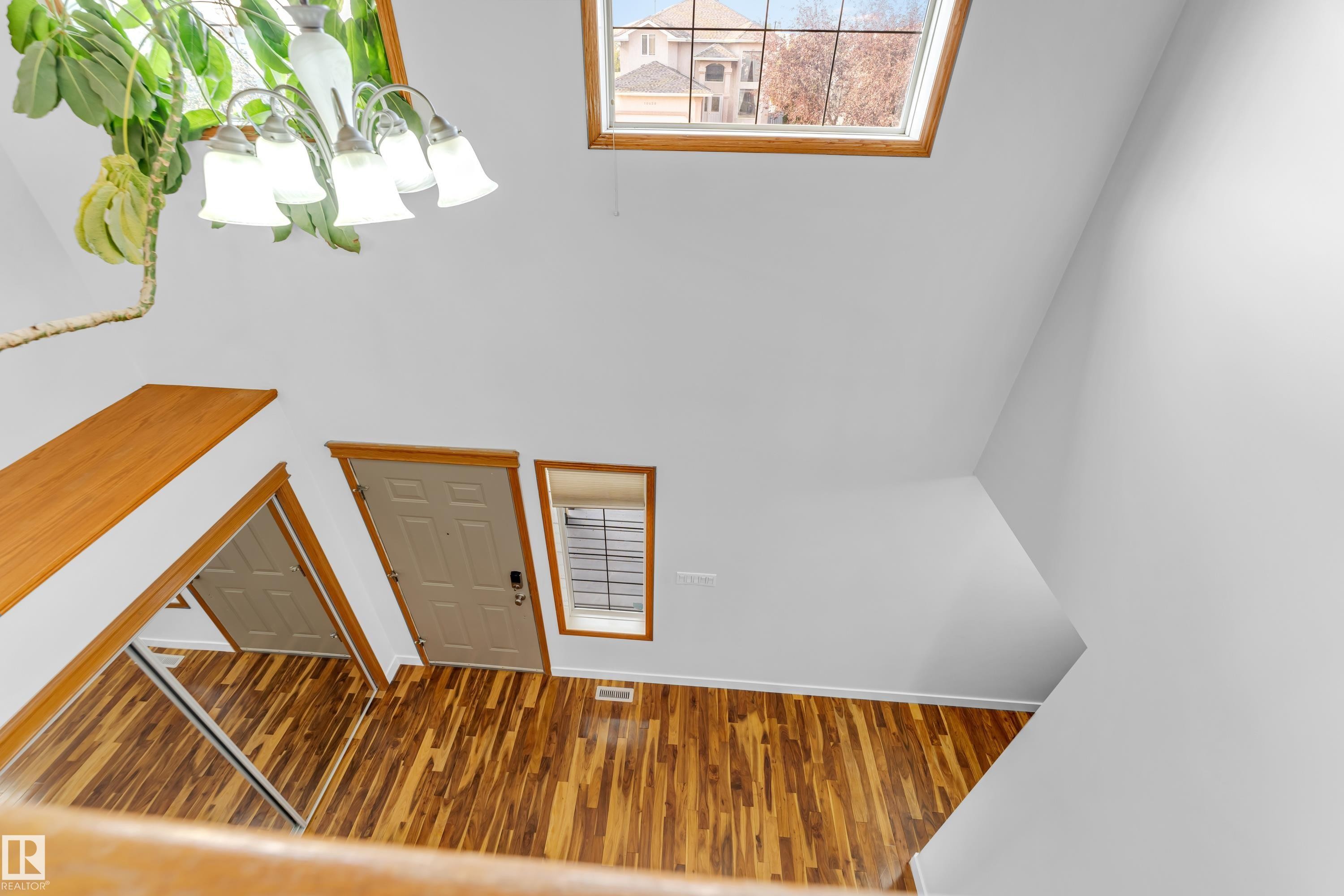 Two-story entry featuring wood-finish flooring, a contemporary chandelier, a windowed door, and an upper-level skylight - 10621 175A Avenue, Edmonton, AB