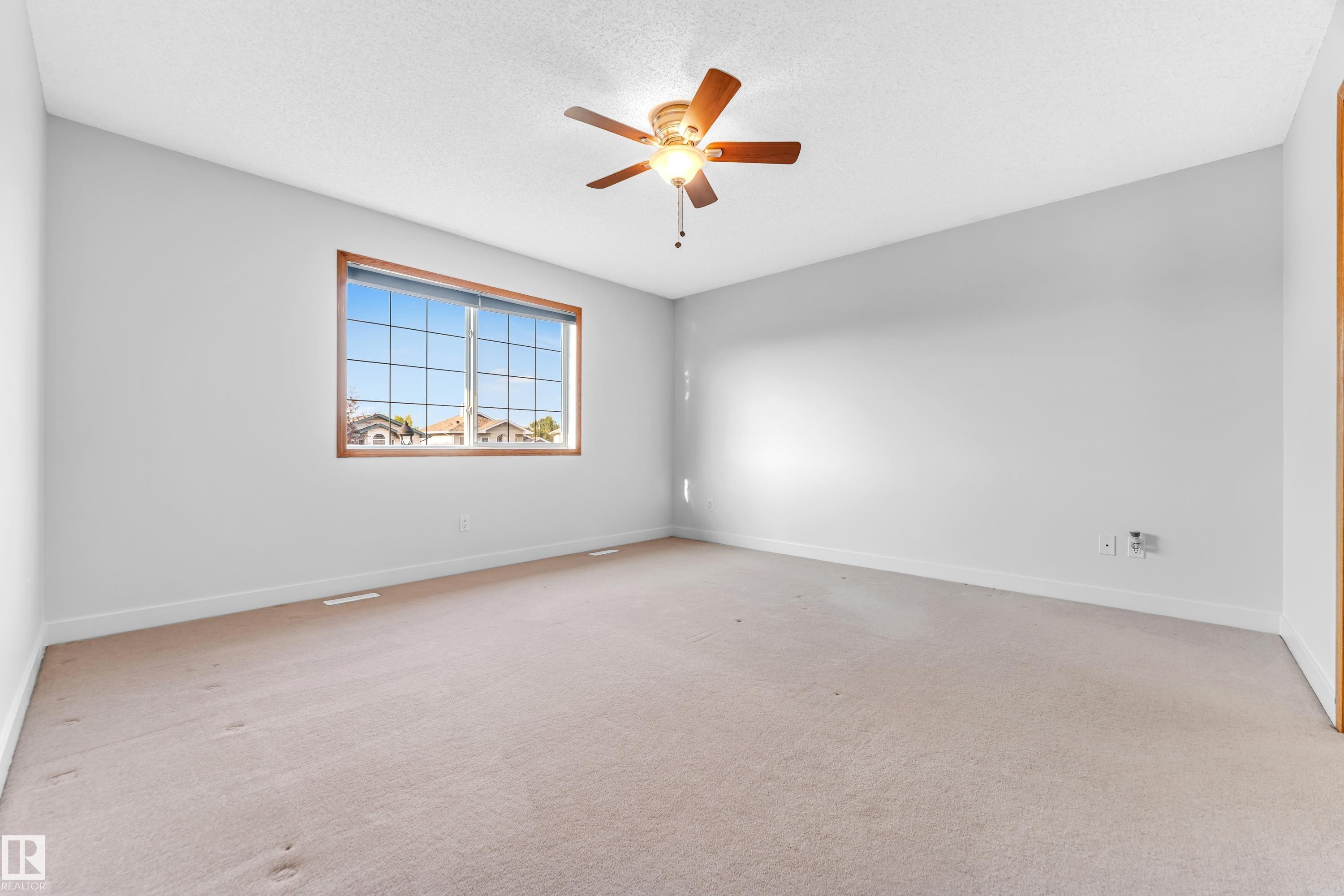 Spacious room featuring neutral wall tones, textured ceiling, a ceiling fan with wood-finish blades, and a large window with a wood-finish frame - 10621 175A Avenue, Edmonton, AB
