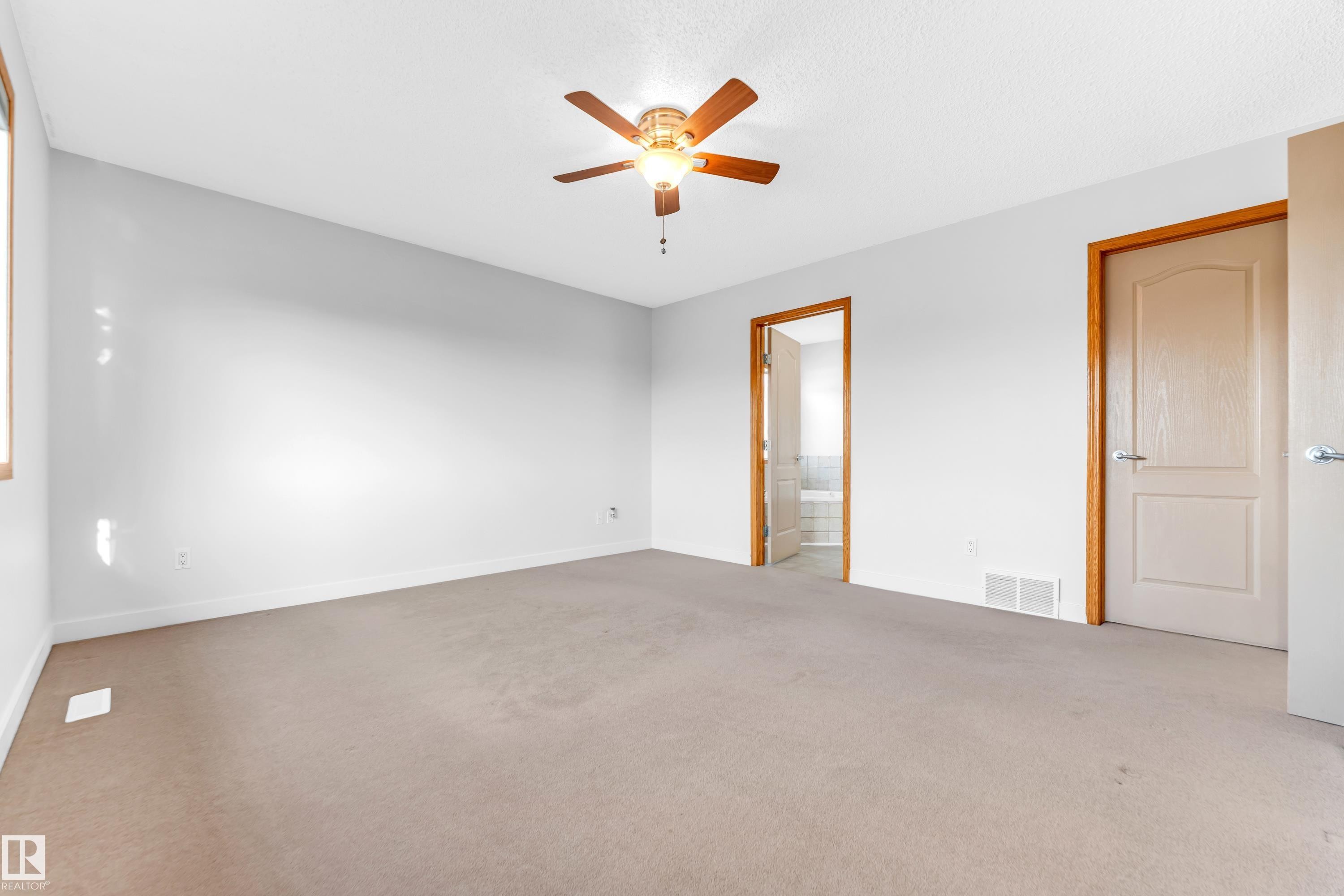 Spacious interior room featuring light neutral wall paint, light-colored carpeting, and a ceiling fan with light fixture - 10621 175A Avenue, Edmonton, AB