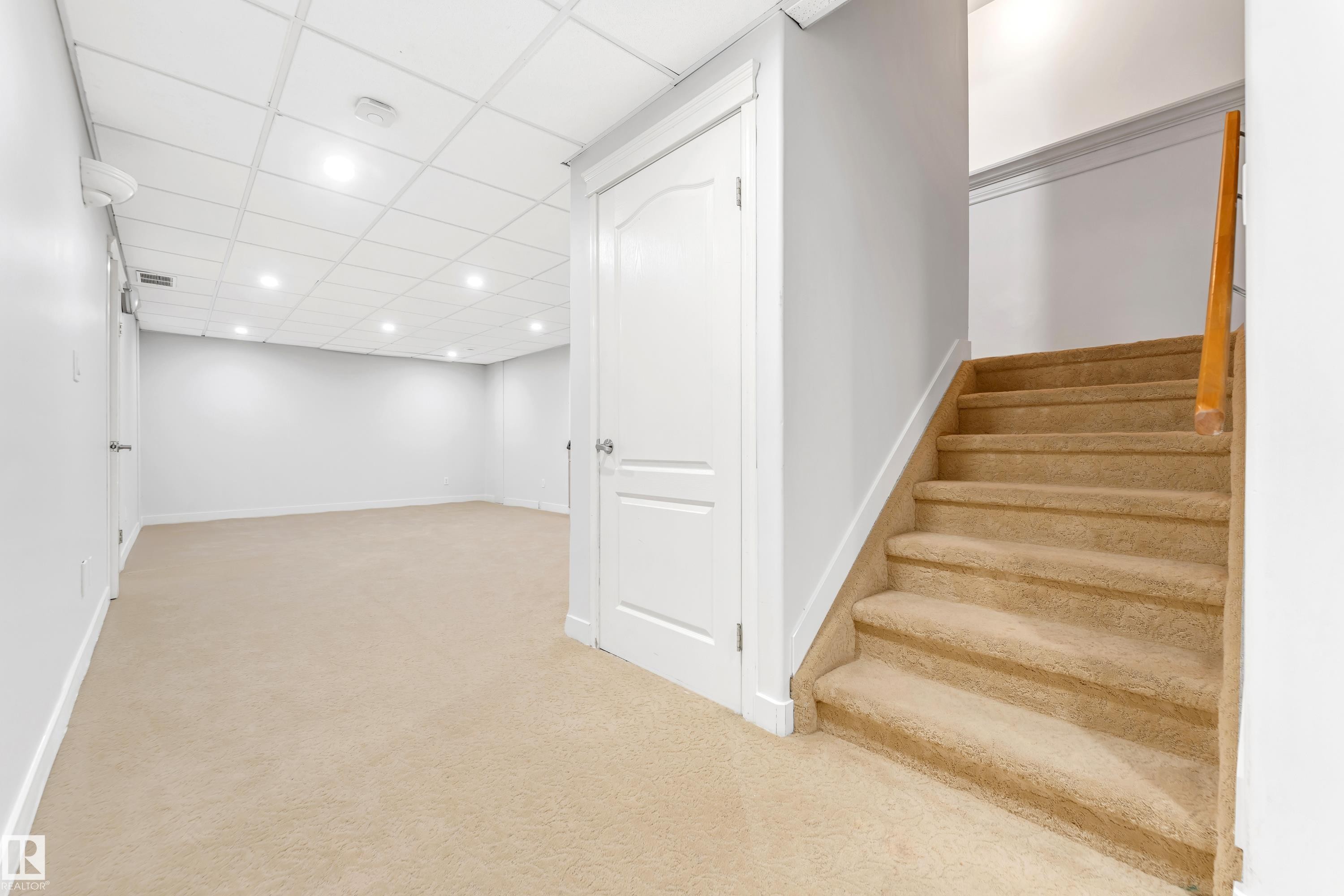 Carpeted staircase with wooden handrail, white walls, and a drop ceiling featuring recessed lighting - 10621 175A Avenue, Edmonton, AB