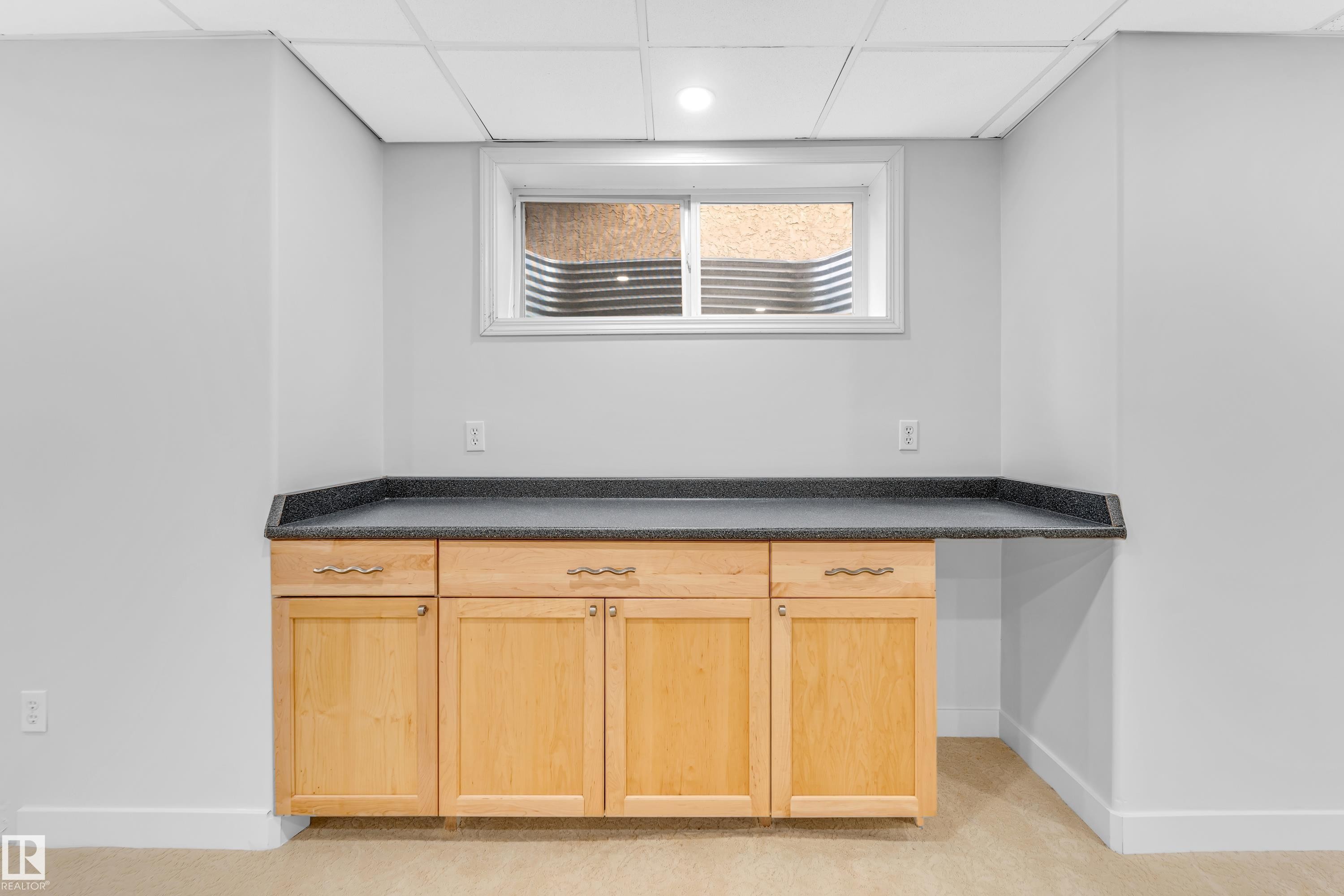 Built-in cabinetry with wood-finish doors and drawers, dark countertop, and an egress window - 10621 175A Avenue, Edmonton, AB