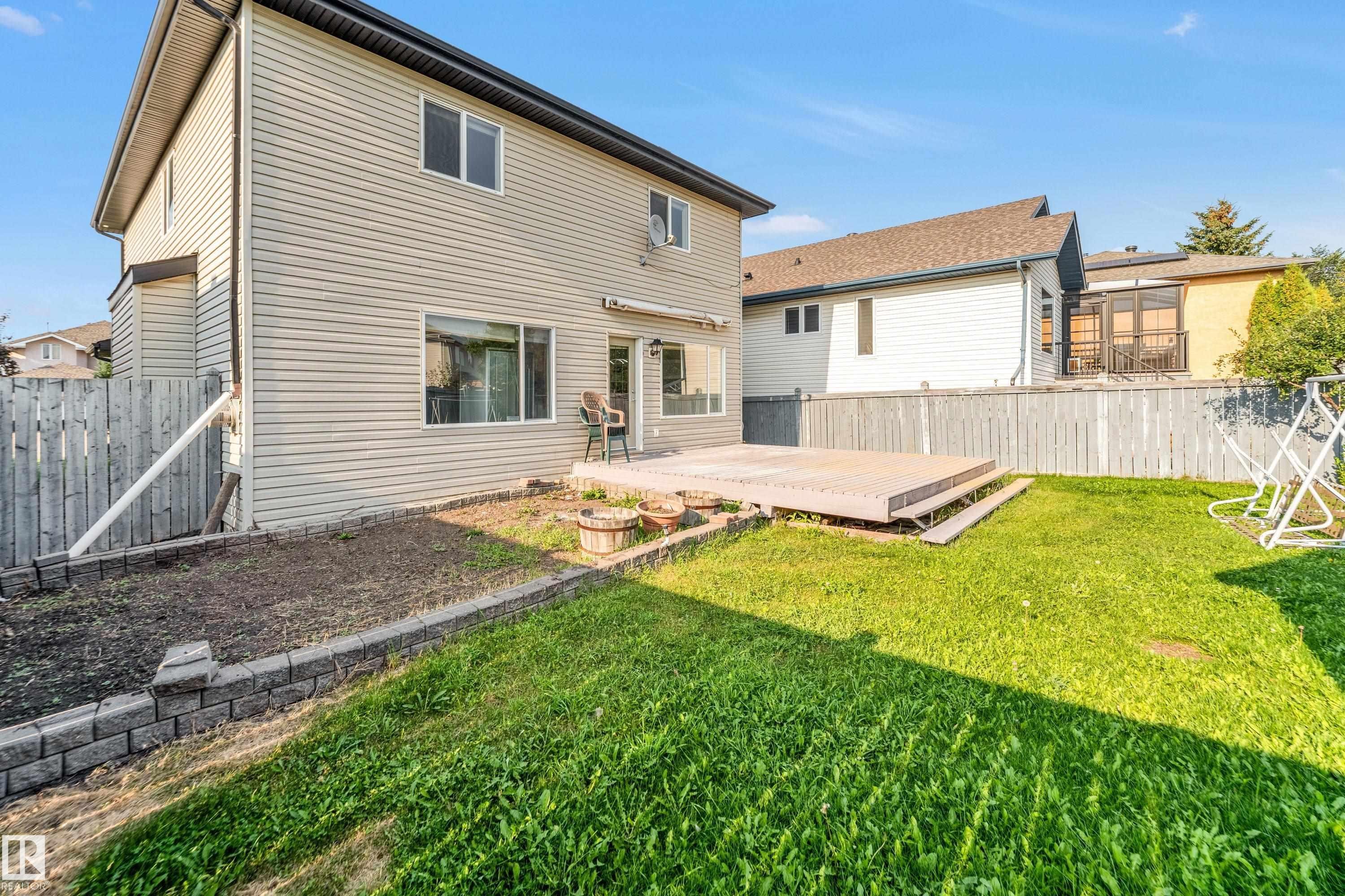Spacious backyard featuring a multi-level deck, expansive lawn, and a retaining wall with planting beds - 10621 175A Avenue, Edmonton, AB