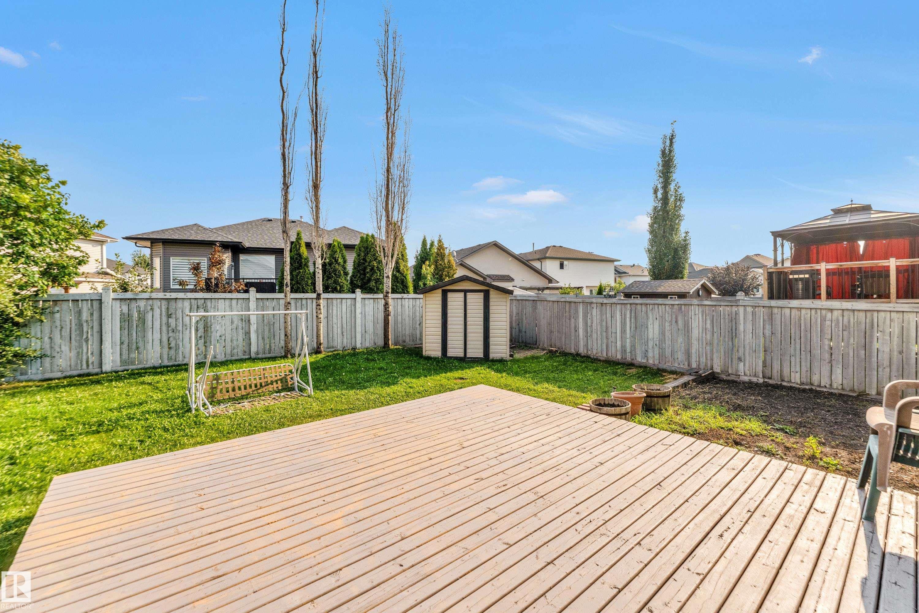 Expansive backyard featuring a spacious wooden deck, manicured lawn, full privacy fencing, and a functional storage shed - 10621 175A Avenue, Edmonton, AB