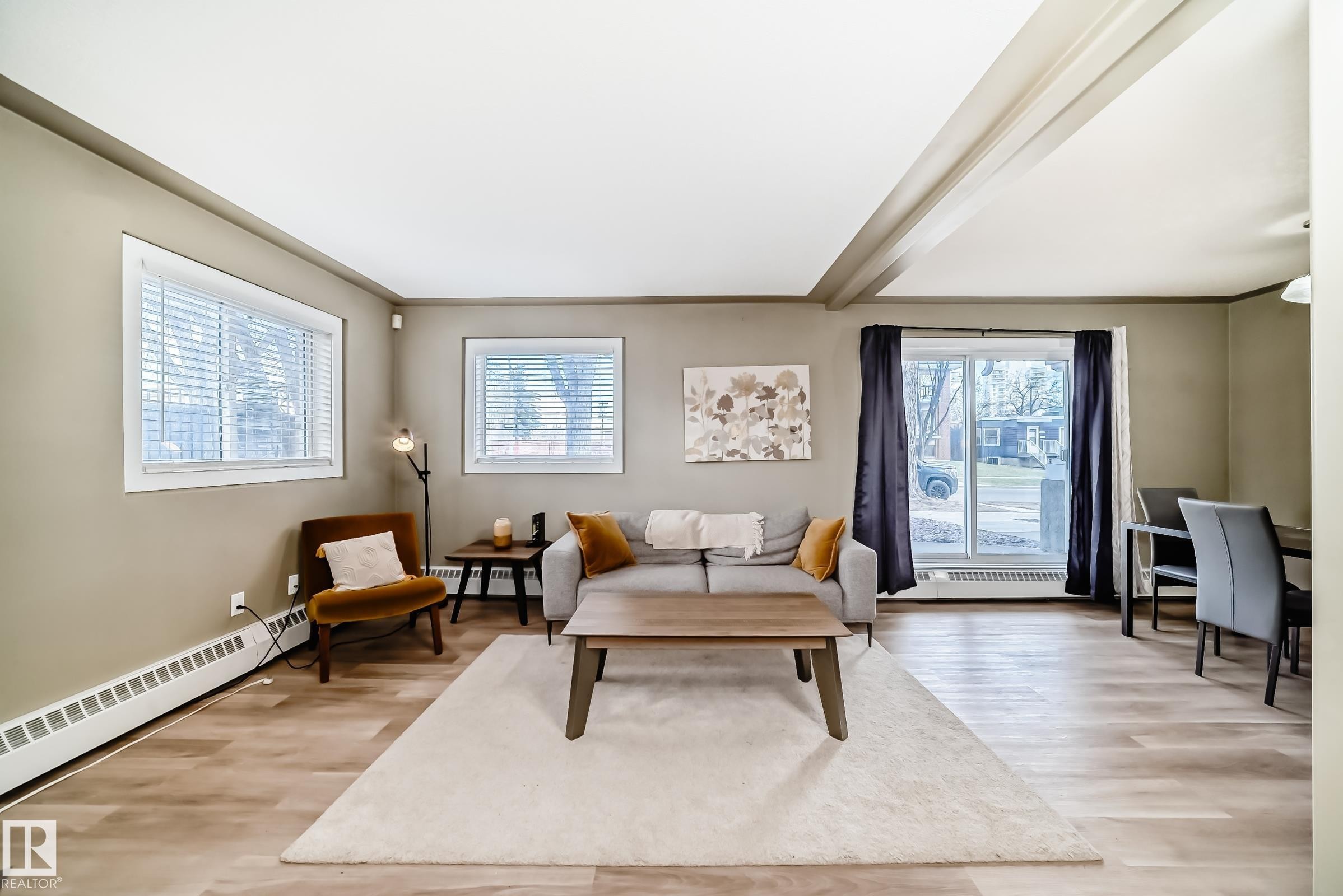 Open-concept living area featuring wood-finish flooring, a sliding glass door, and multiple windows - 101 10827 85 Avenue Nw, Edmonton, AB - Indoor Photo Showing Living Room