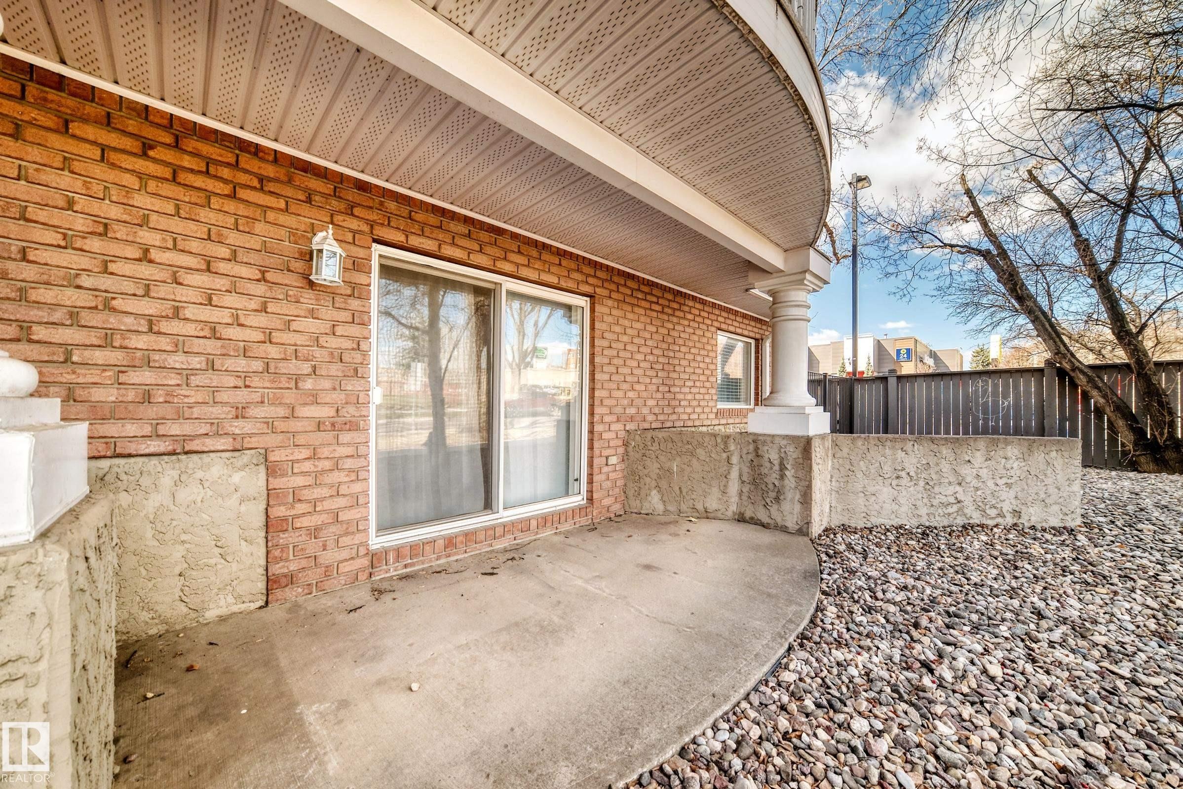 Brick exterior with a concrete patio, sliding glass door, and white architectural columns - 101 10827 85 Avenue Nw, Edmonton, AB - Outdoor With Exterior