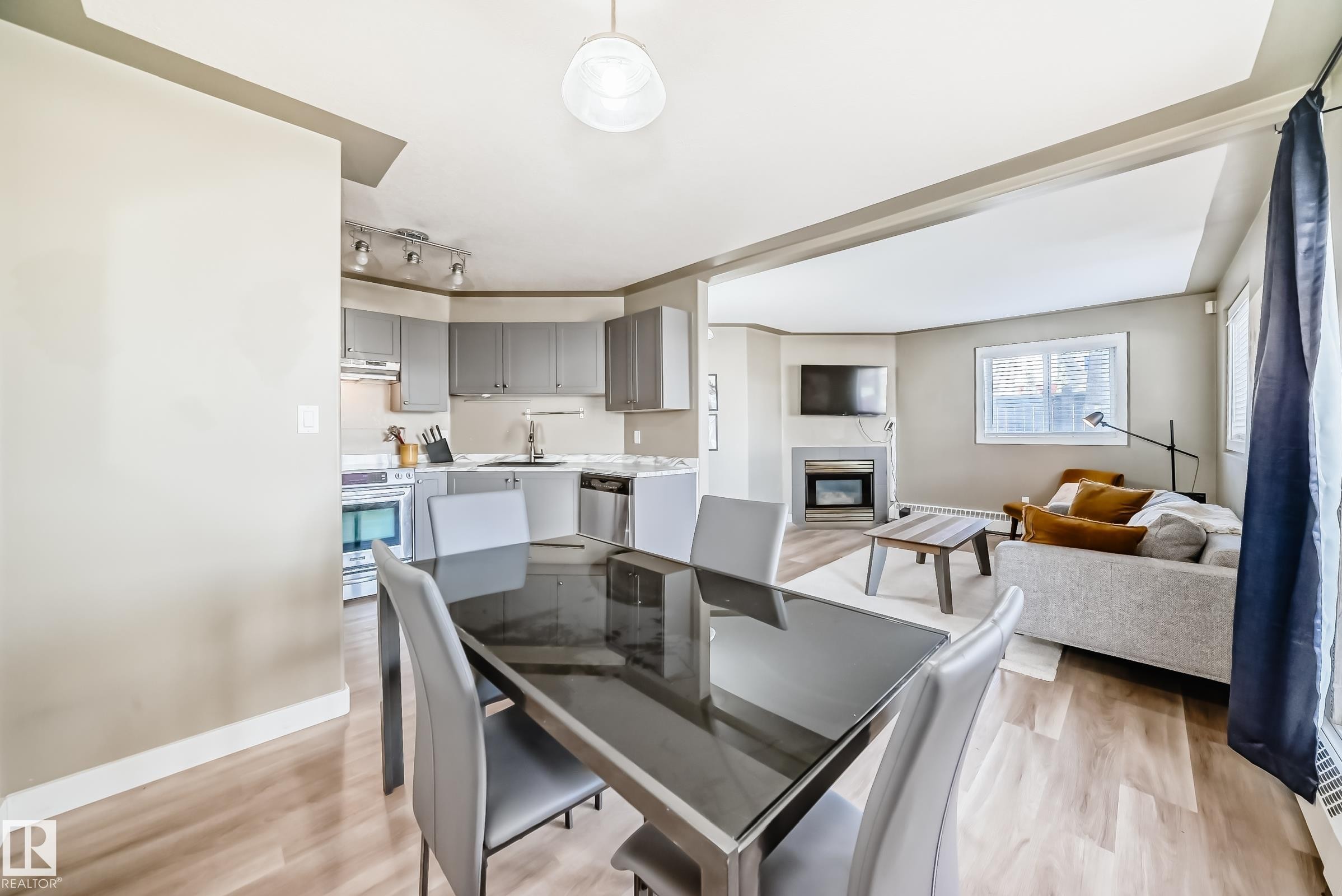 Open-concept dining area featuring wood-finish flooring, a contemporary overhead light fixture, and a clear line of sight to the kitchen and living room - 101 10827 85 Avenue Nw, Edmonton, AB - Indoor With Fireplace