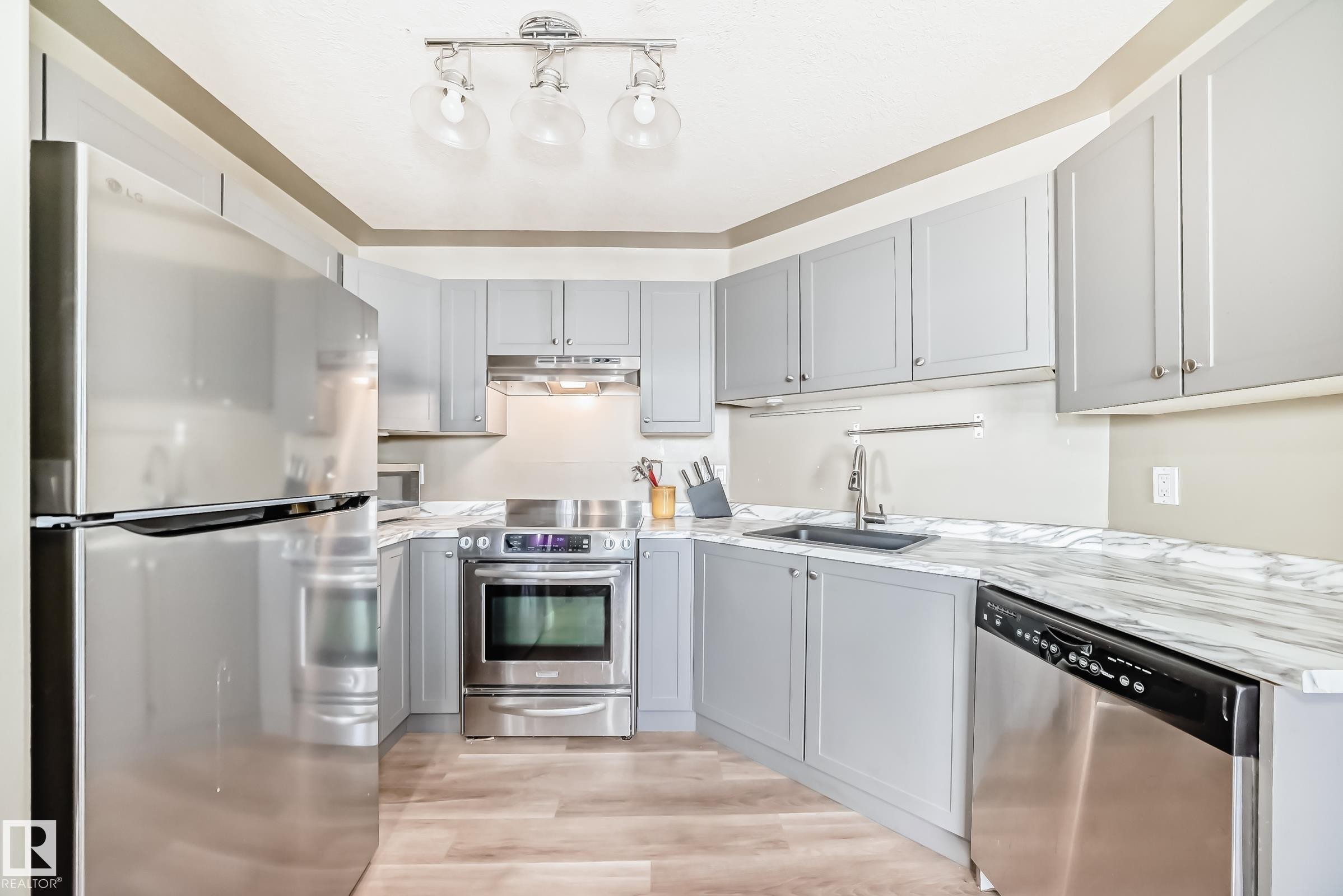 Kitchen featuring light gray cabinetry, stainless steel appliances, marble-look countertops, a black undermount sink, and wood-finish flooring - 101 10827 85 Avenue Nw, Edmonton, AB - Indoor Photo Showing Kitchen With Upgraded Kitchen