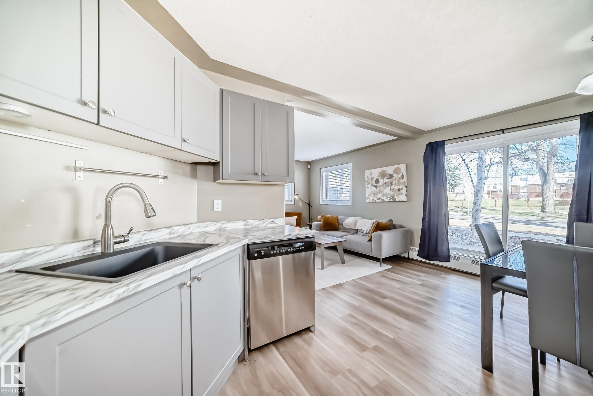 Modern kitchen with light grey cabinetry, a stainless steel dishwasher, and a black composite sink with a gooseneck faucet - 101 10827 85 Avenue Nw, Edmonton, AB - Indoor Photo Showing Kitchen