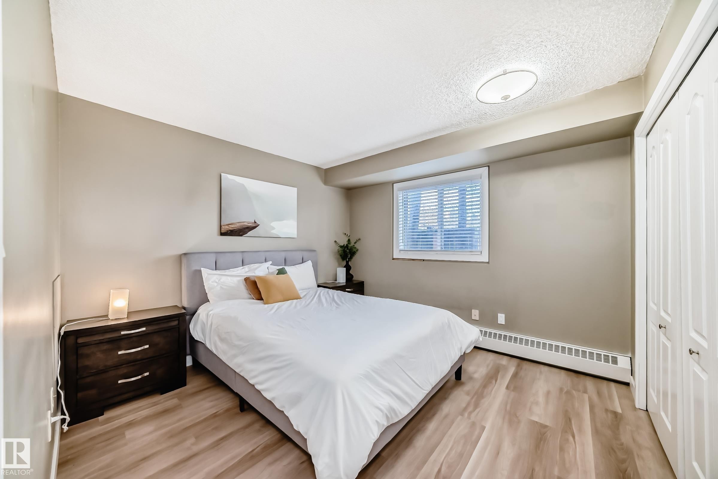 Bedroom featuring light wood-finish flooring, neutral wall tones, a window with horizontal blinds, and a built-in bi-fold door closet - 101 10827 85 Avenue Nw, Edmonton, AB - Indoor Photo Showing Bedroom