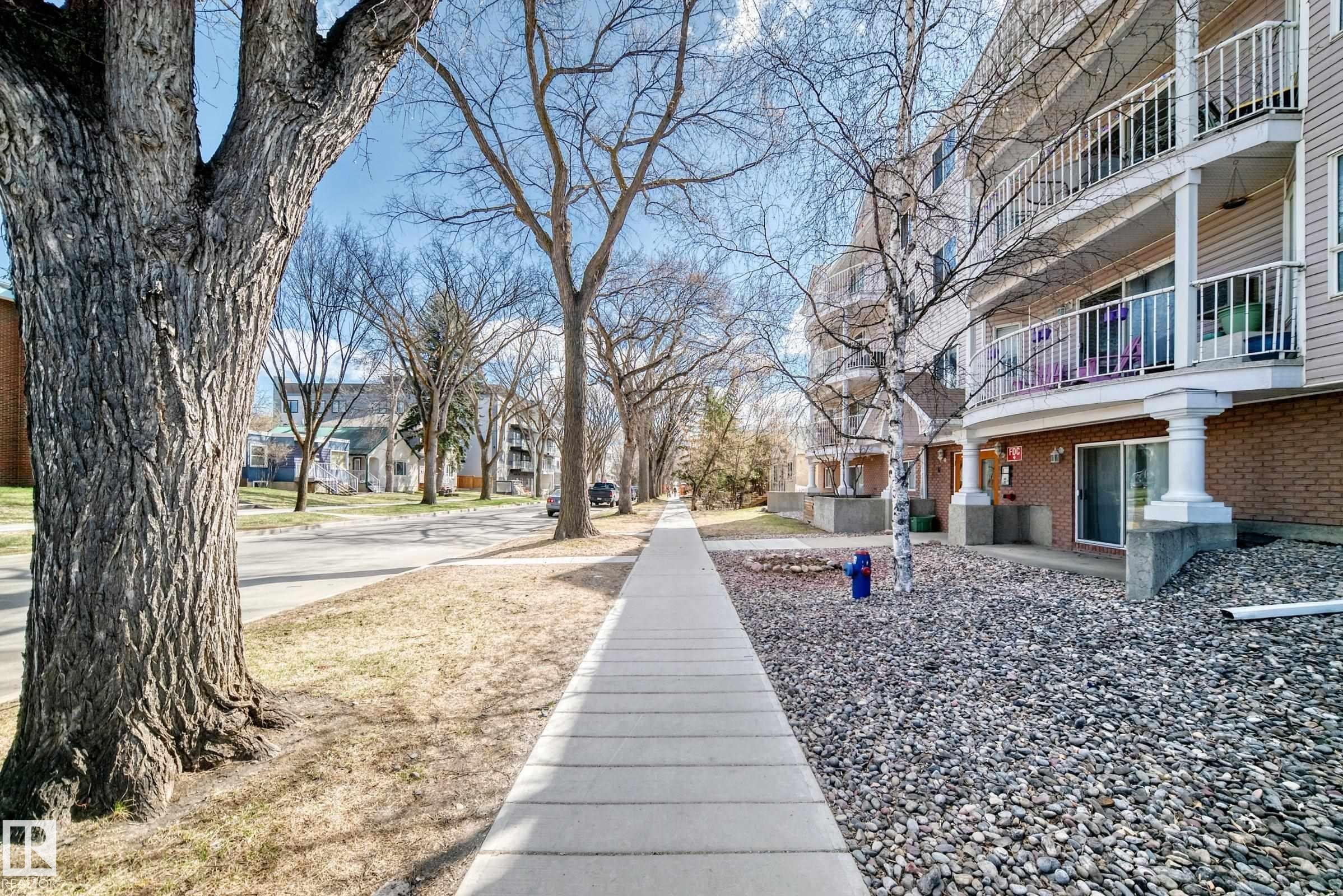 Multi-story building featuring tan horizontal siding, white balcony railings, and ground-level sliding patio doors - 101 10827 85 Avenue Nw, Edmonton, AB - Outdoor