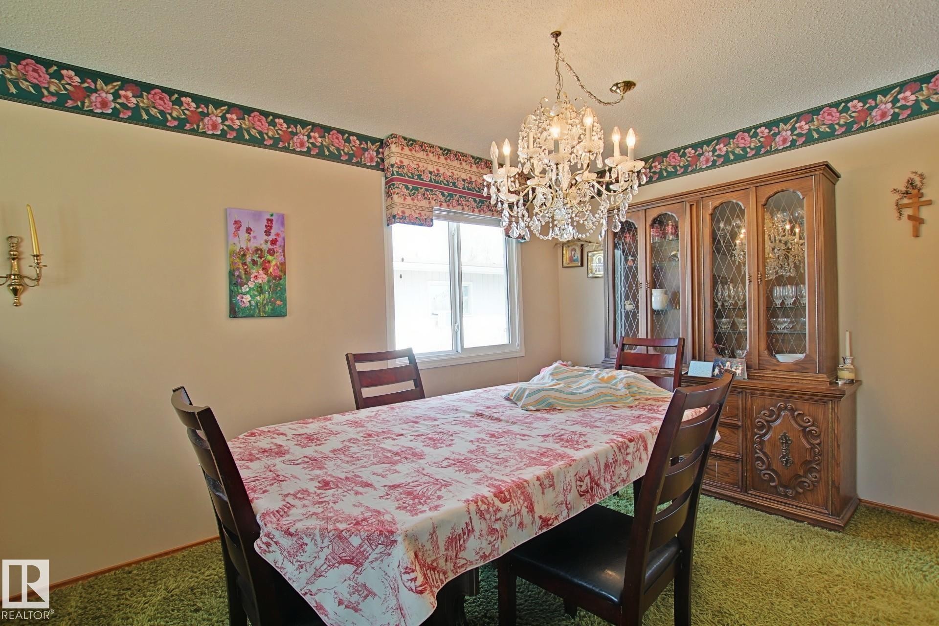 Dining space featuring a crystal chandelier, a large window, wall-mounted sconces, and green carpeting - 3539 104 Street, Edmonton, AB - Indoor Photo Showing Dining Room