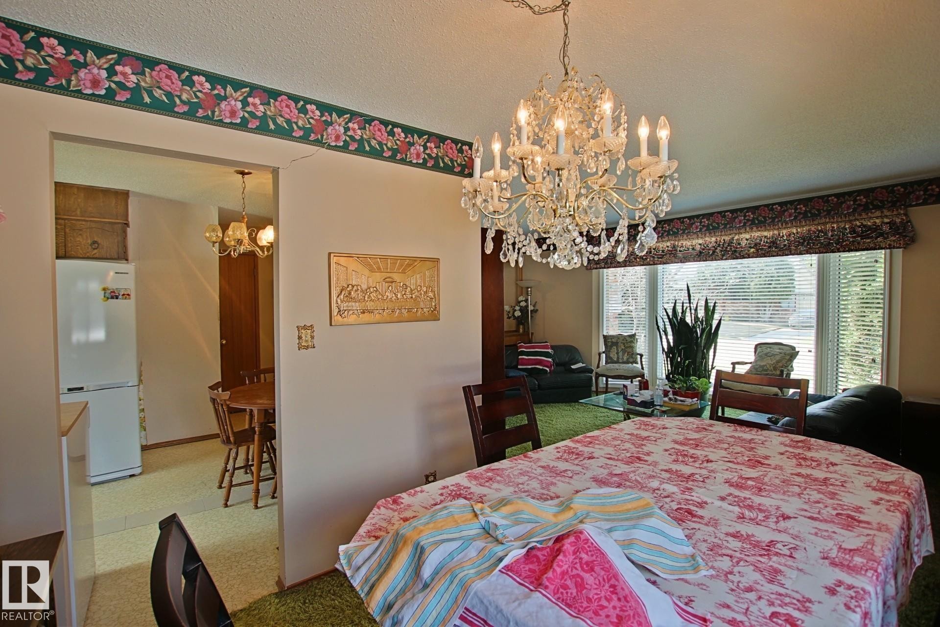 Dining area featuring a crystal chandelier, patterned wallpaper border, and broad window with blinds - 3539 104 Street, Edmonton, AB - Indoor