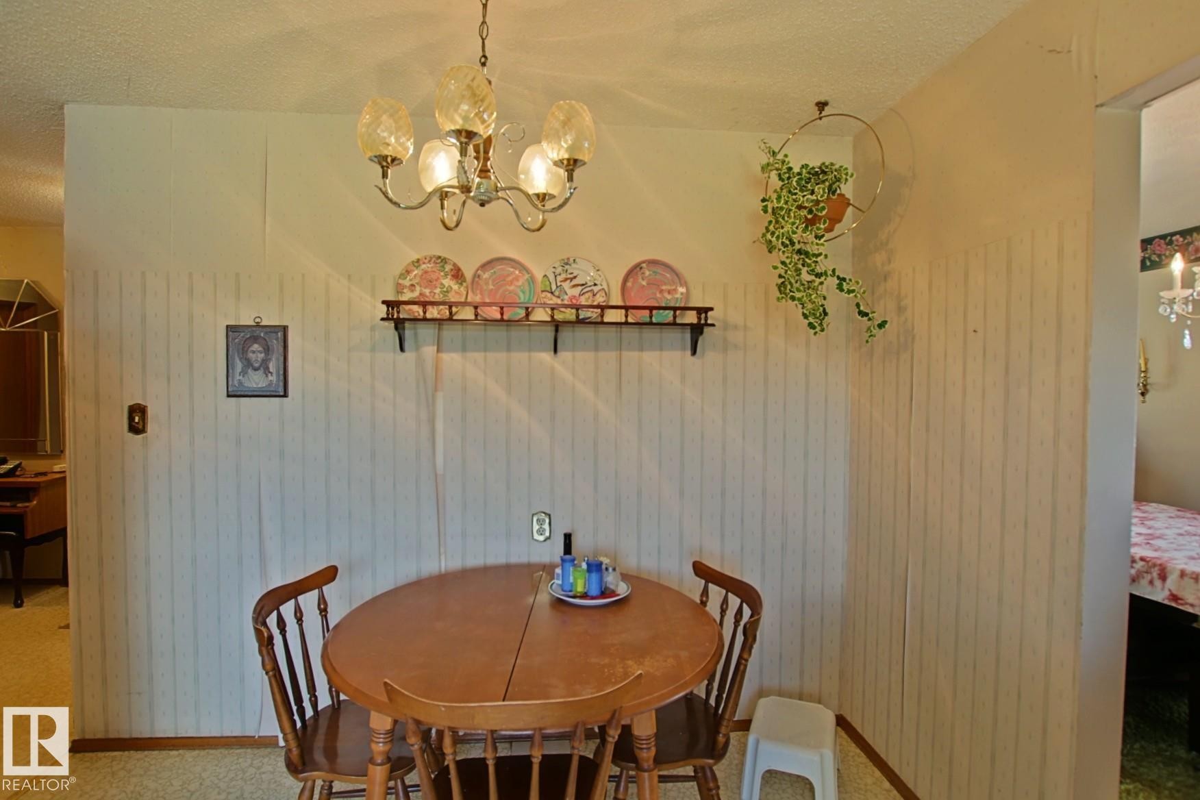 Dining area featuring a brass-tone chandelier with fluted glass shades, wood-finish flooring, and light-toned vertical stripe wallpaper - 3539 104 Street, Edmonton, AB - Indoor Photo Showing Dining Room