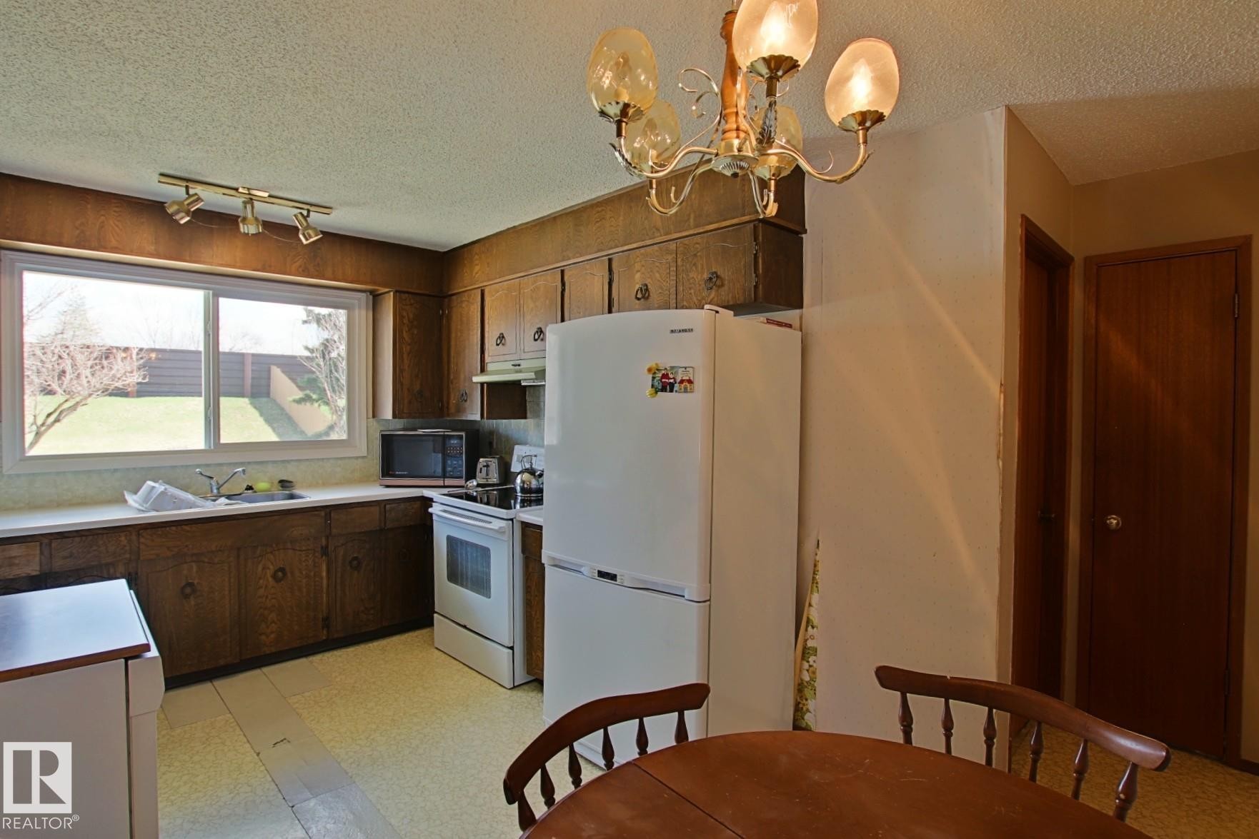 Kitchen featuring wood-finish cabinetry, a double-basin sink, and a large window overlooking the backyard - 3539 104 Street, Edmonton, AB - Indoor Photo Showing Other Room