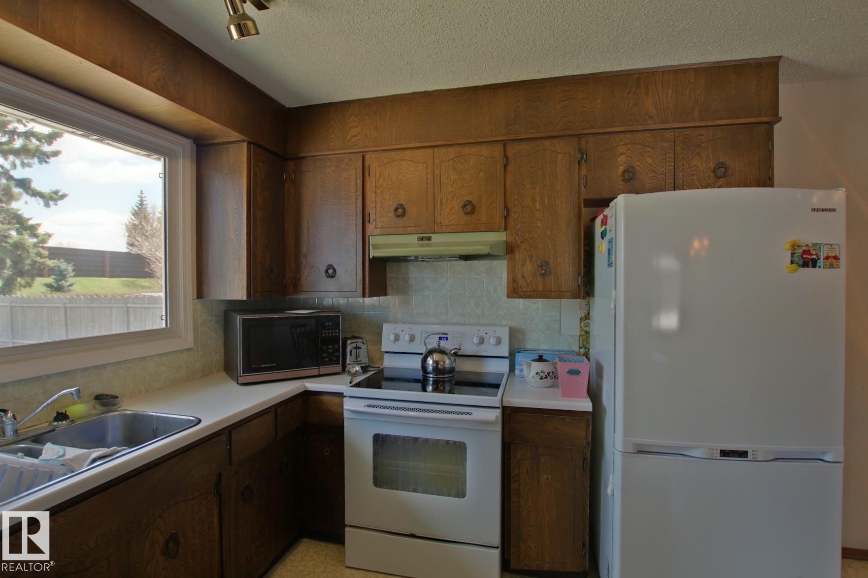 Kitchen featuring wood-finish cabinetry, white countertops, and a stainless steel sink - 3539 104 Street, Edmonton, AB - Indoor Photo Showing Kitchen With Double Sink