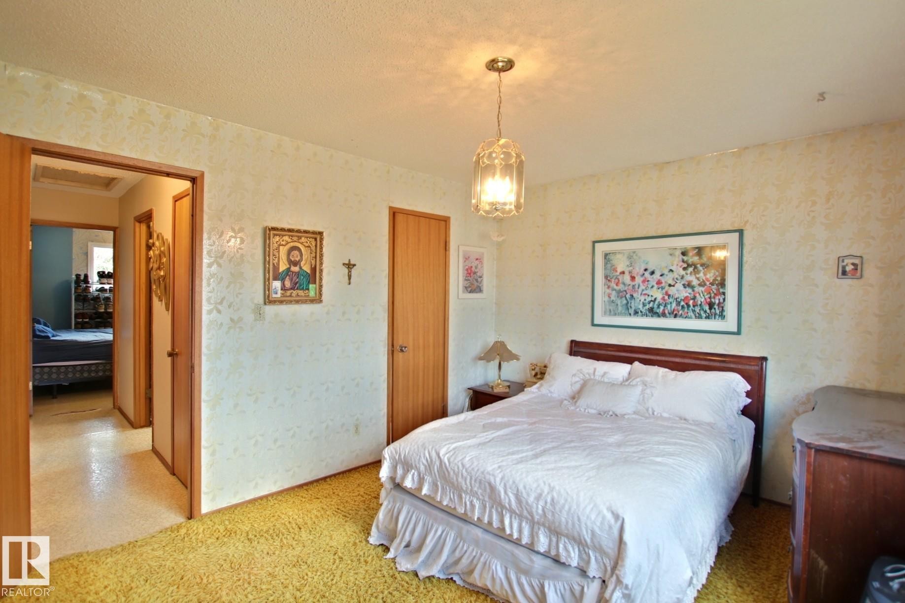 Bedroom featuring textured wallpaper, plush carpeting, a wood-finish headboard, and a glass pendant light fixture - 3539 104 Street, Edmonton, AB - Indoor Photo Showing Bedroom