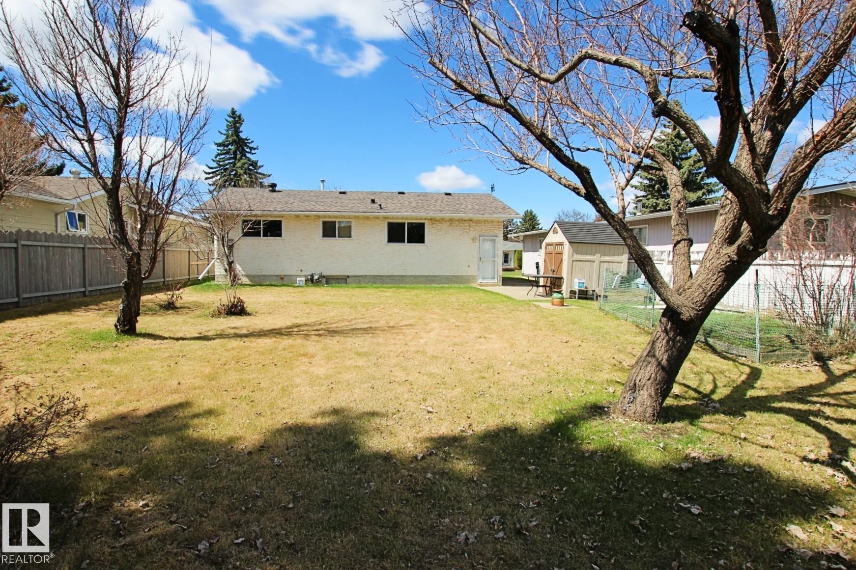 Spacious backyard featuring an expansive lawn, mature trees, a storage shed, and a concrete patio area - 3539 104 Street, Edmonton, AB - Outdoor
