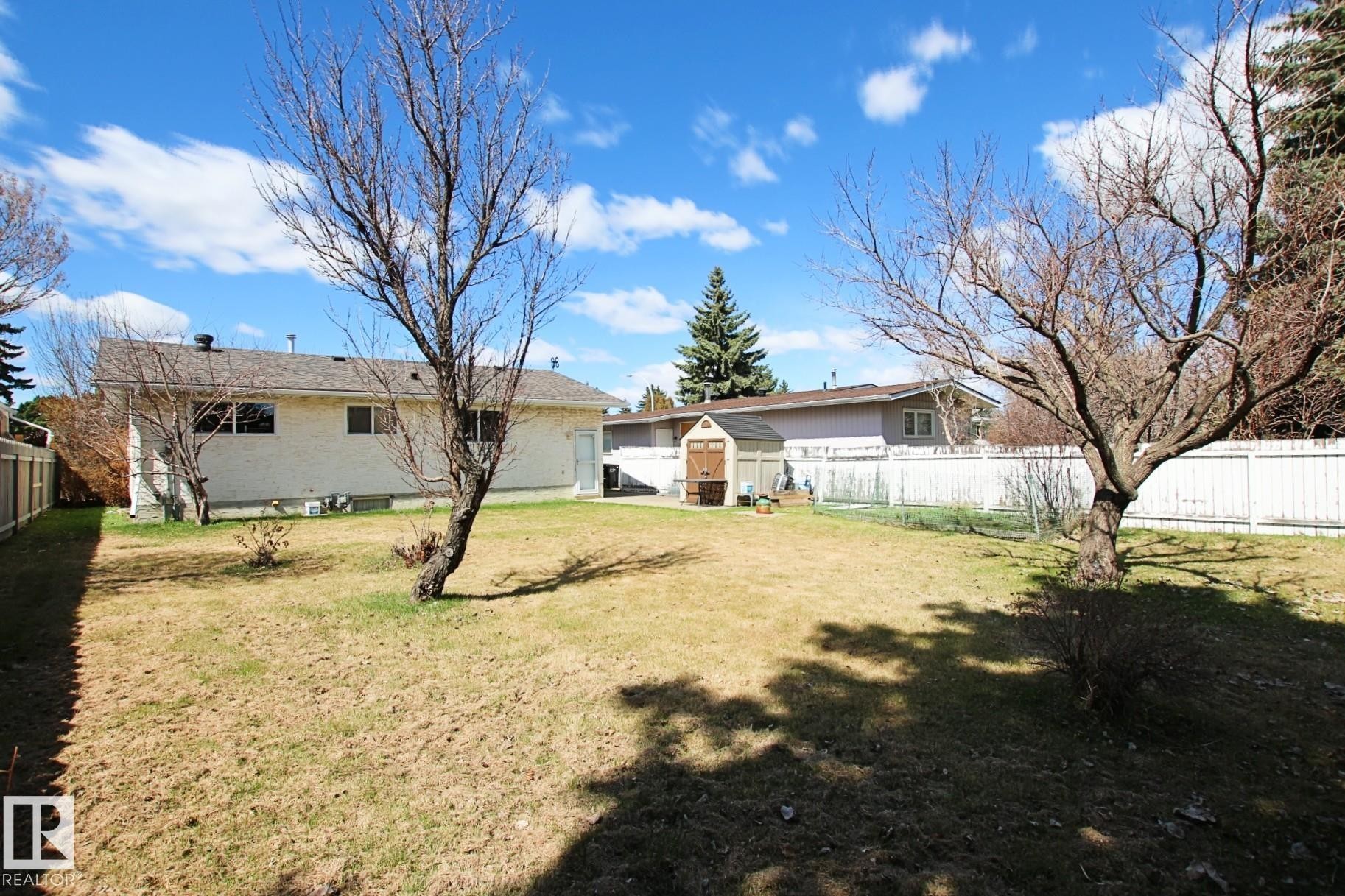 Expansive backyard featuring a partial white privacy fence, two mature deciduous trees, and a functional storage shed - 3539 104 Street, Edmonton, AB - Outdoor